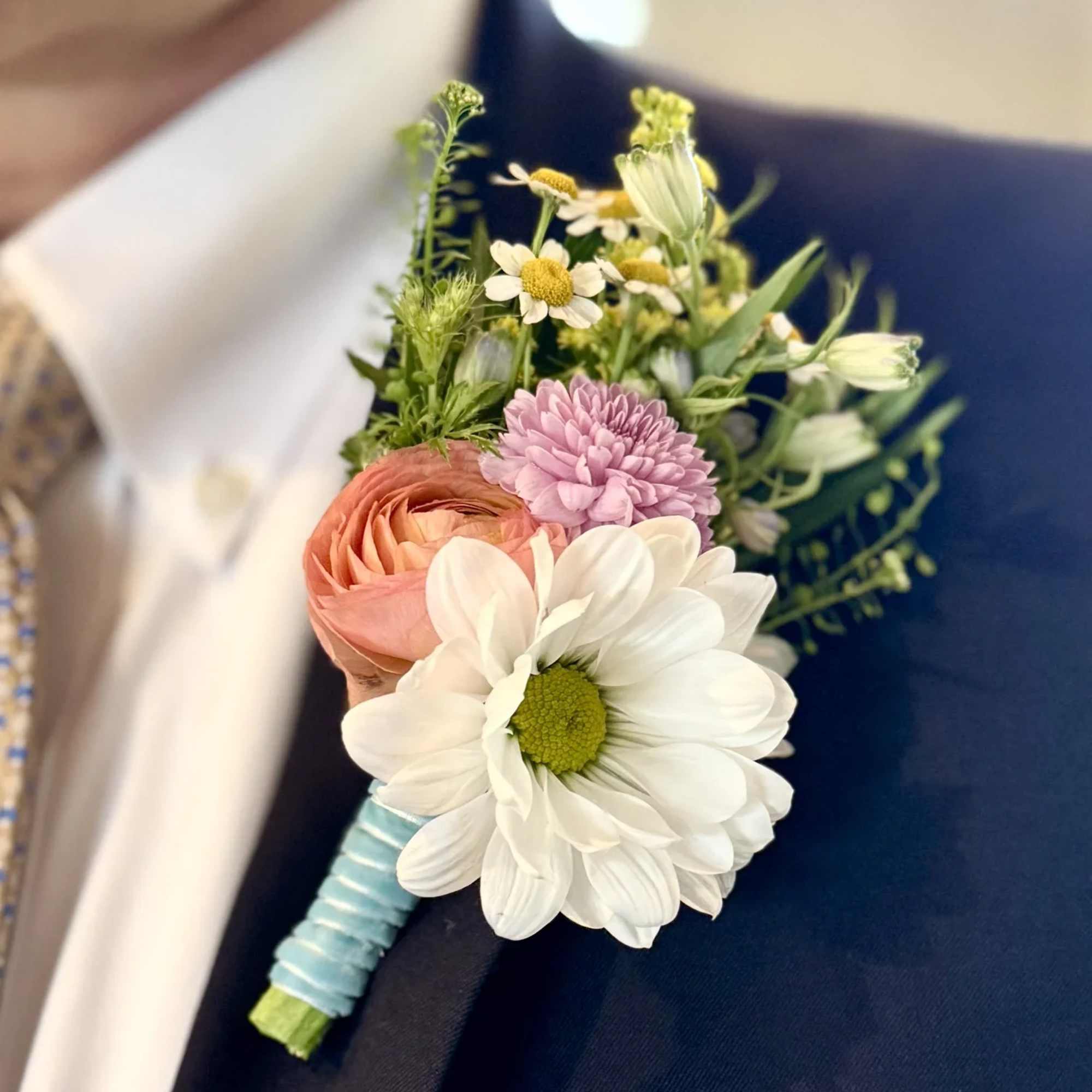 Boutonniere with white daisy, peach ranunculus, and pink bloom