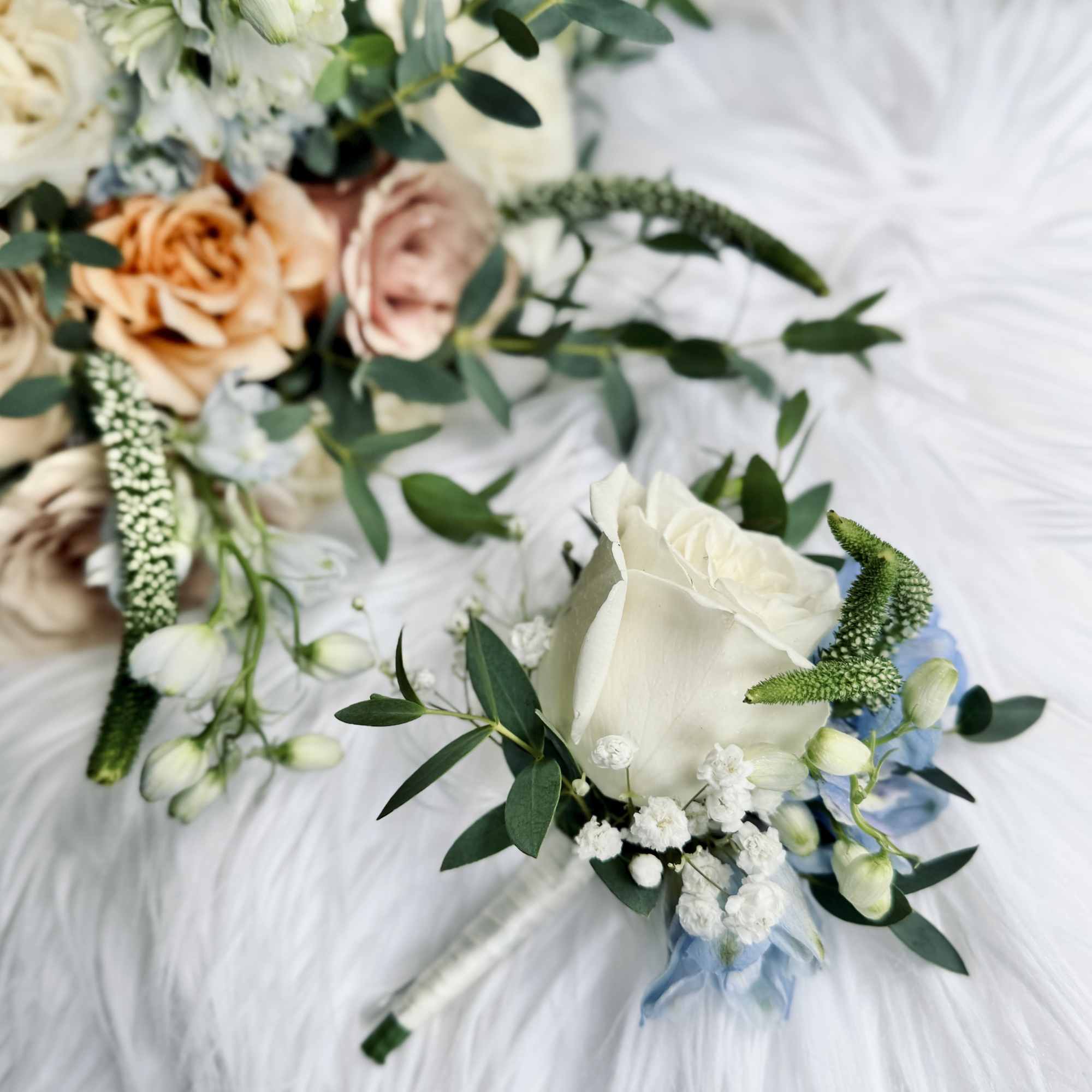 White rose bouquet with blue accents and greenery on a white dress