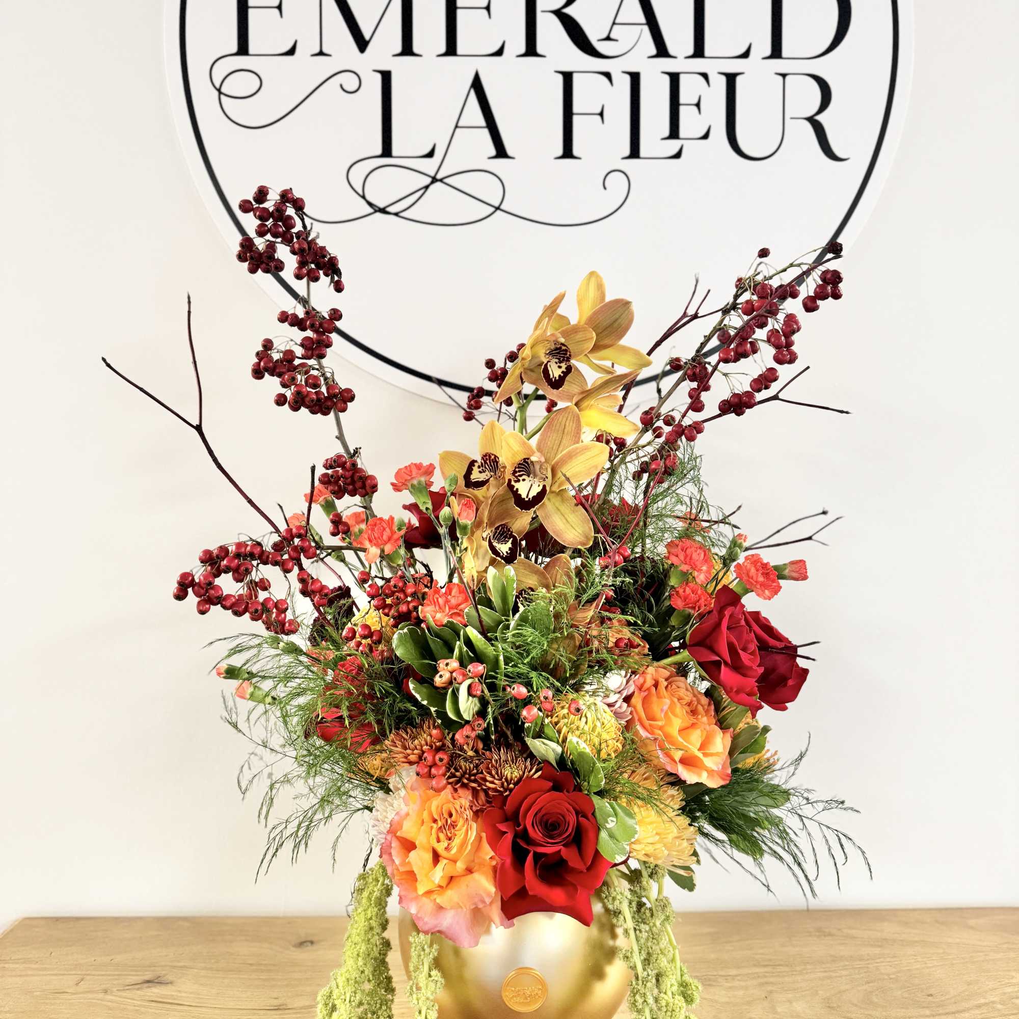 Tall floral arrangement in a gold vase with red, orange, and yellow blooms