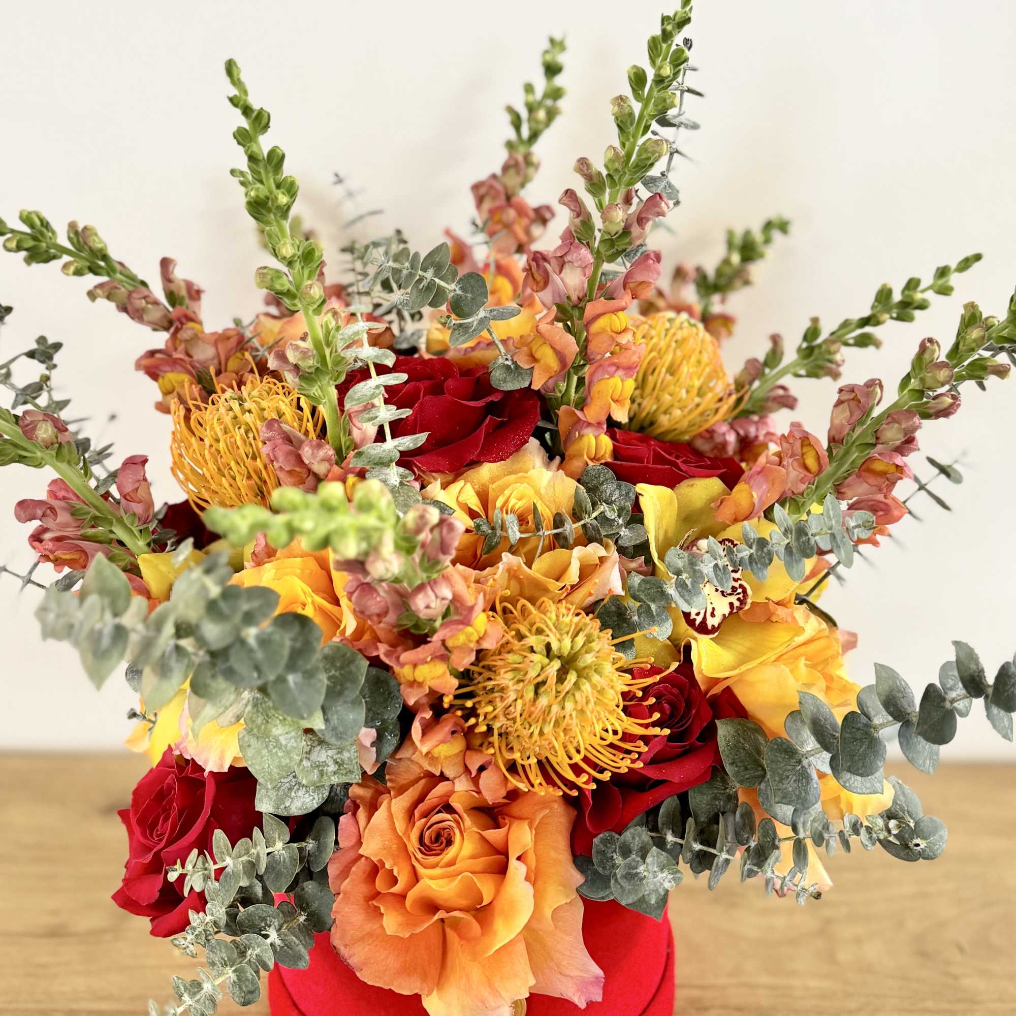 Bouquet of red, orange, and yellow flowers in a red hat box
