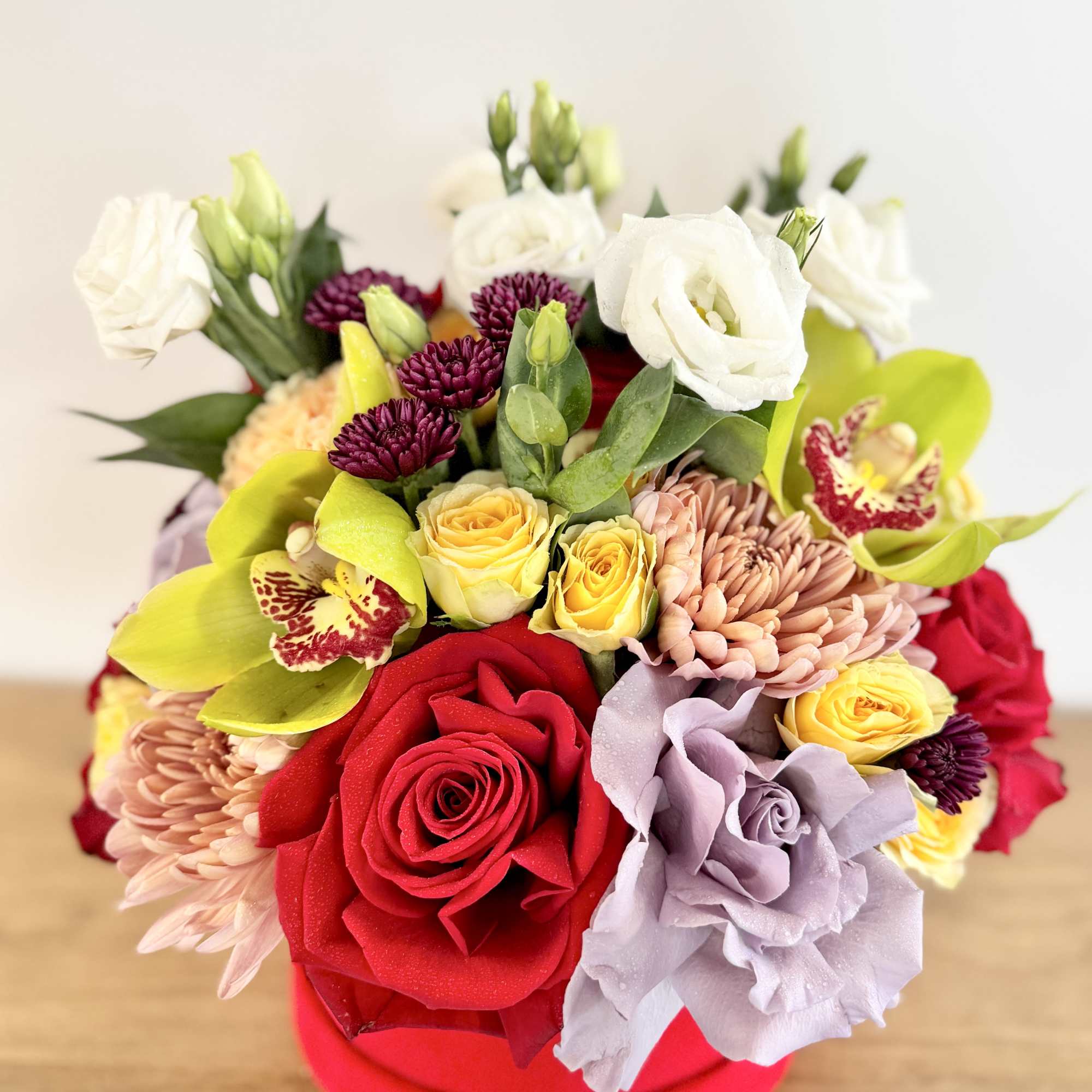 Mixed bouquet of roses, orchids, and chrysanthemums in a red box