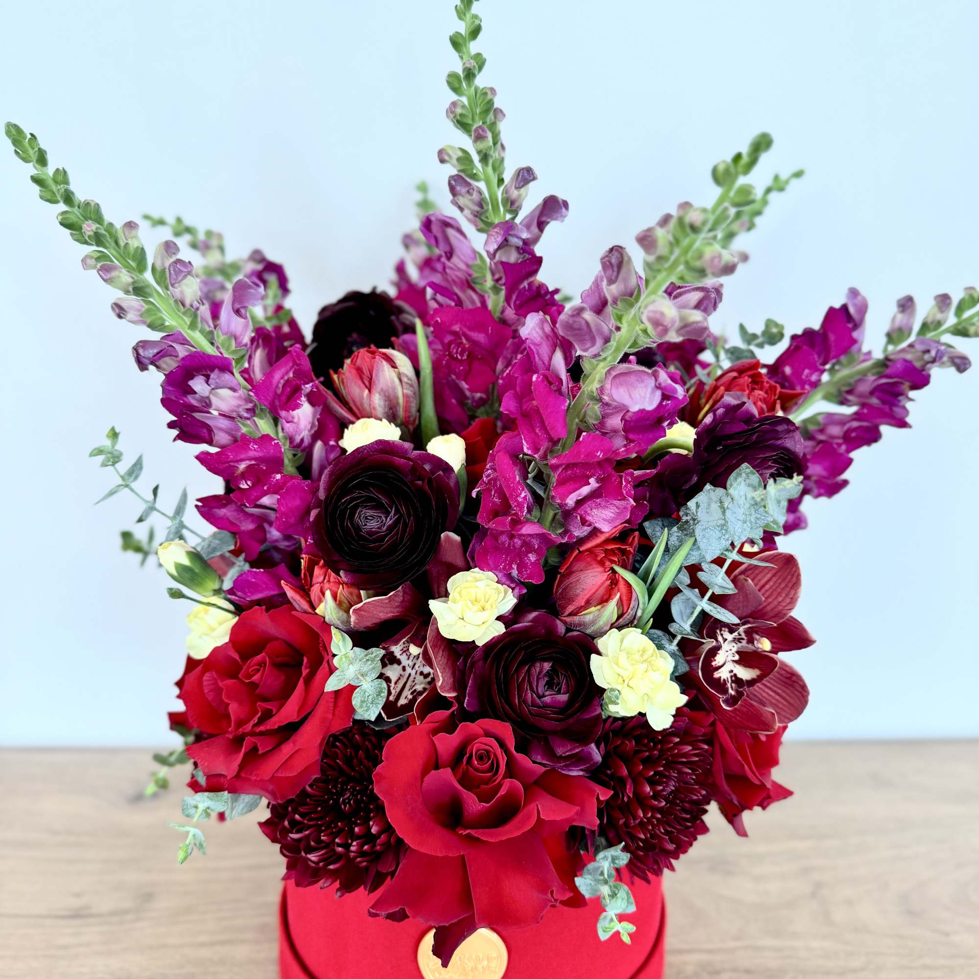 Red and burgundy floral arrangement in a round hat box