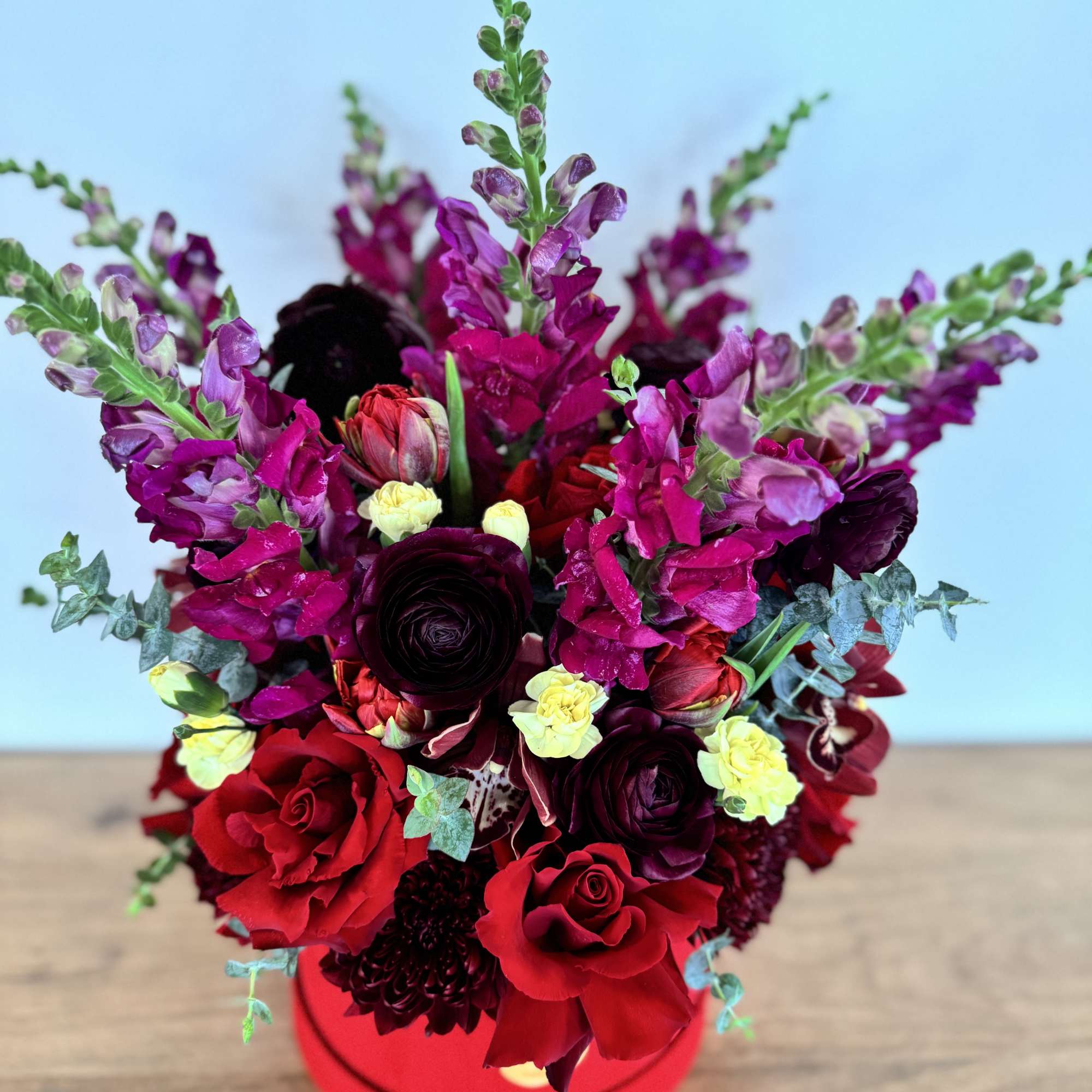 Red and purple floral arrangement in a round red box