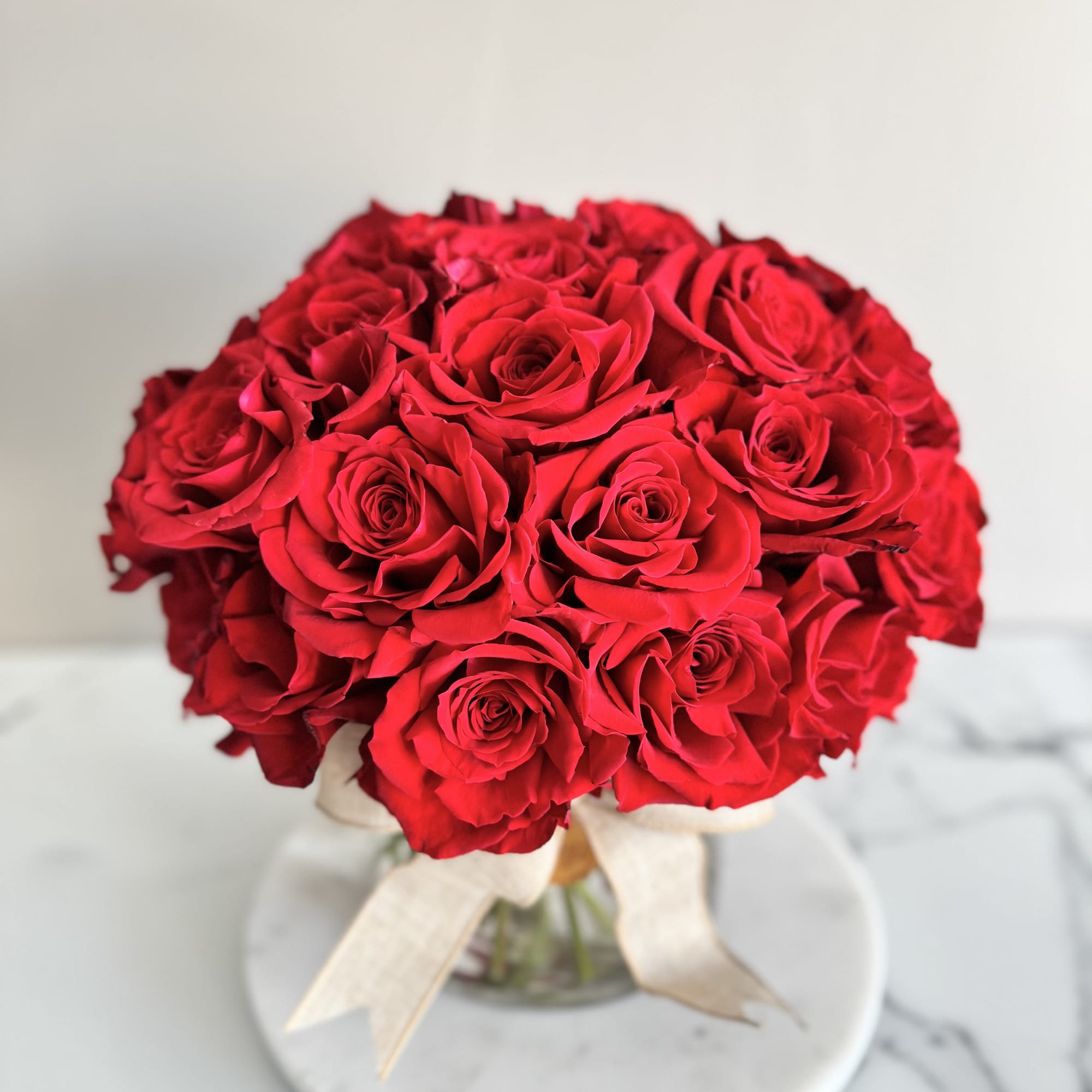 Round bouquet of red roses tied with a cream ribbon
