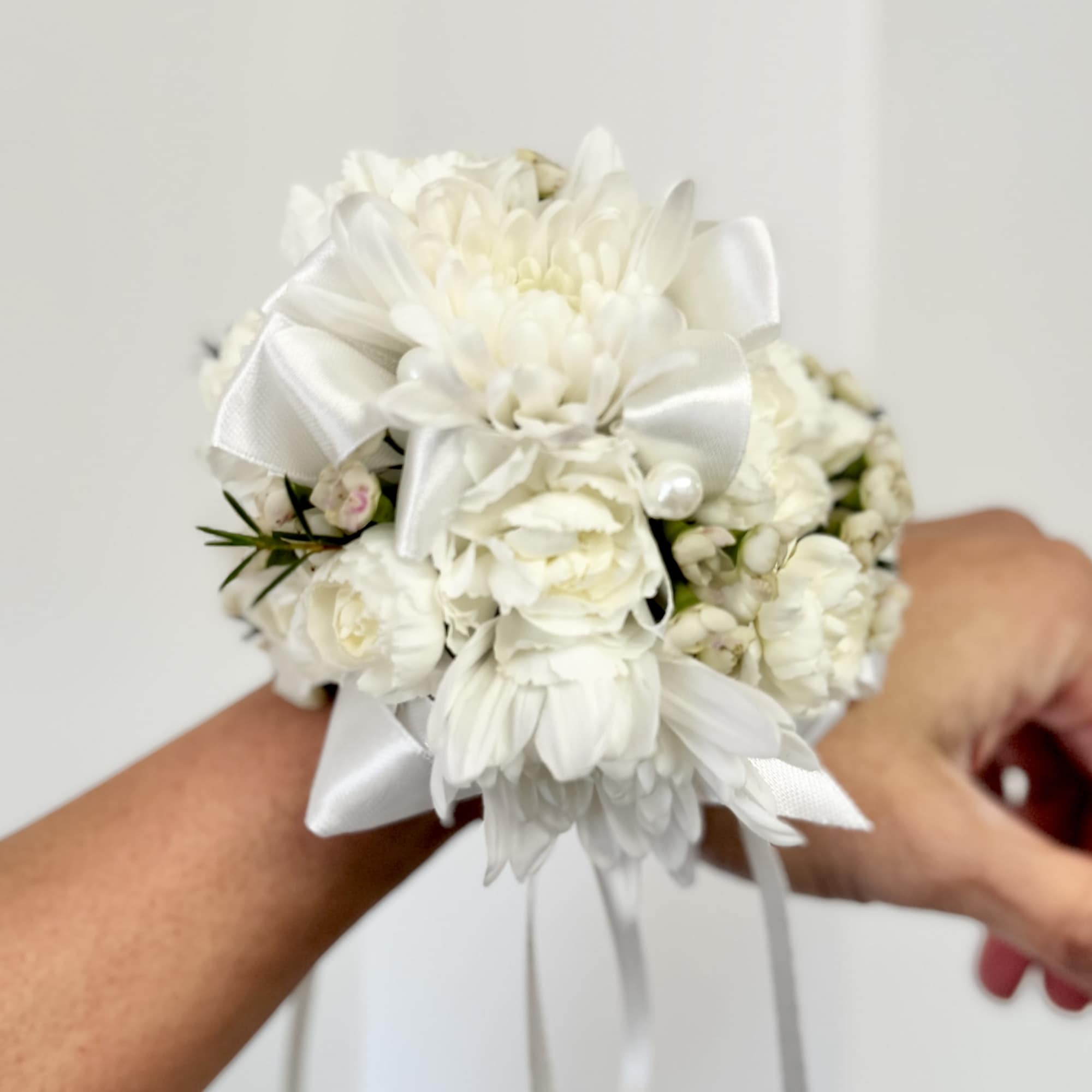 White floral wrist corsage with ribbon and pearl accents
