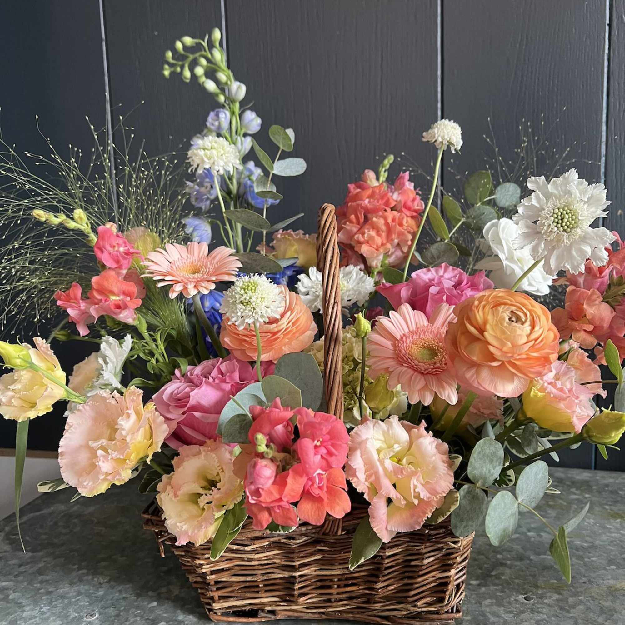 Seasonal, colorful flowers and foliage artfully arranged in a rectangular woven basket.

Year