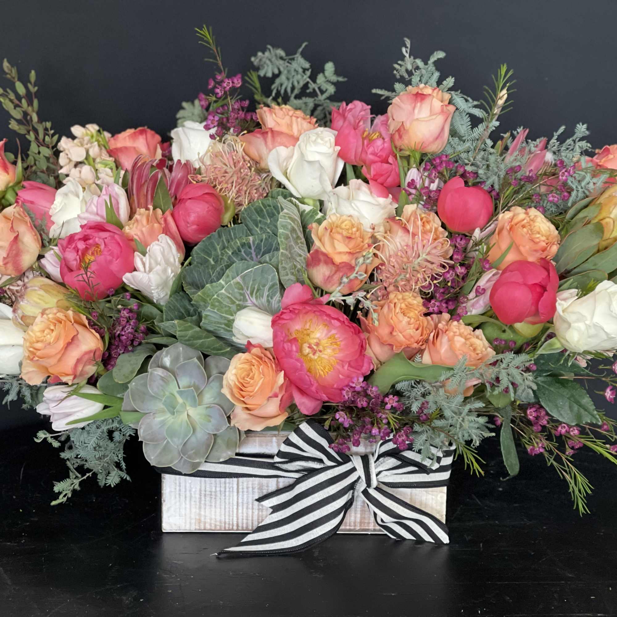 Mixed pink, peach, and white flowers in a striped ribbon box arrangement