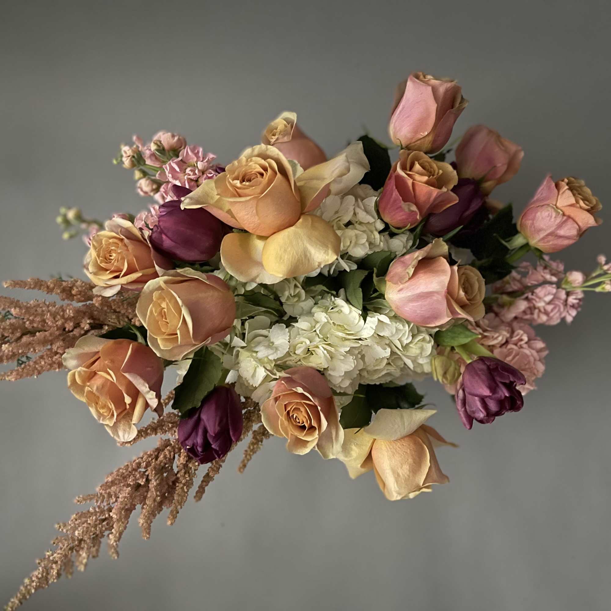 Bouquet of peach, pink, and purple roses with white hydrangeas