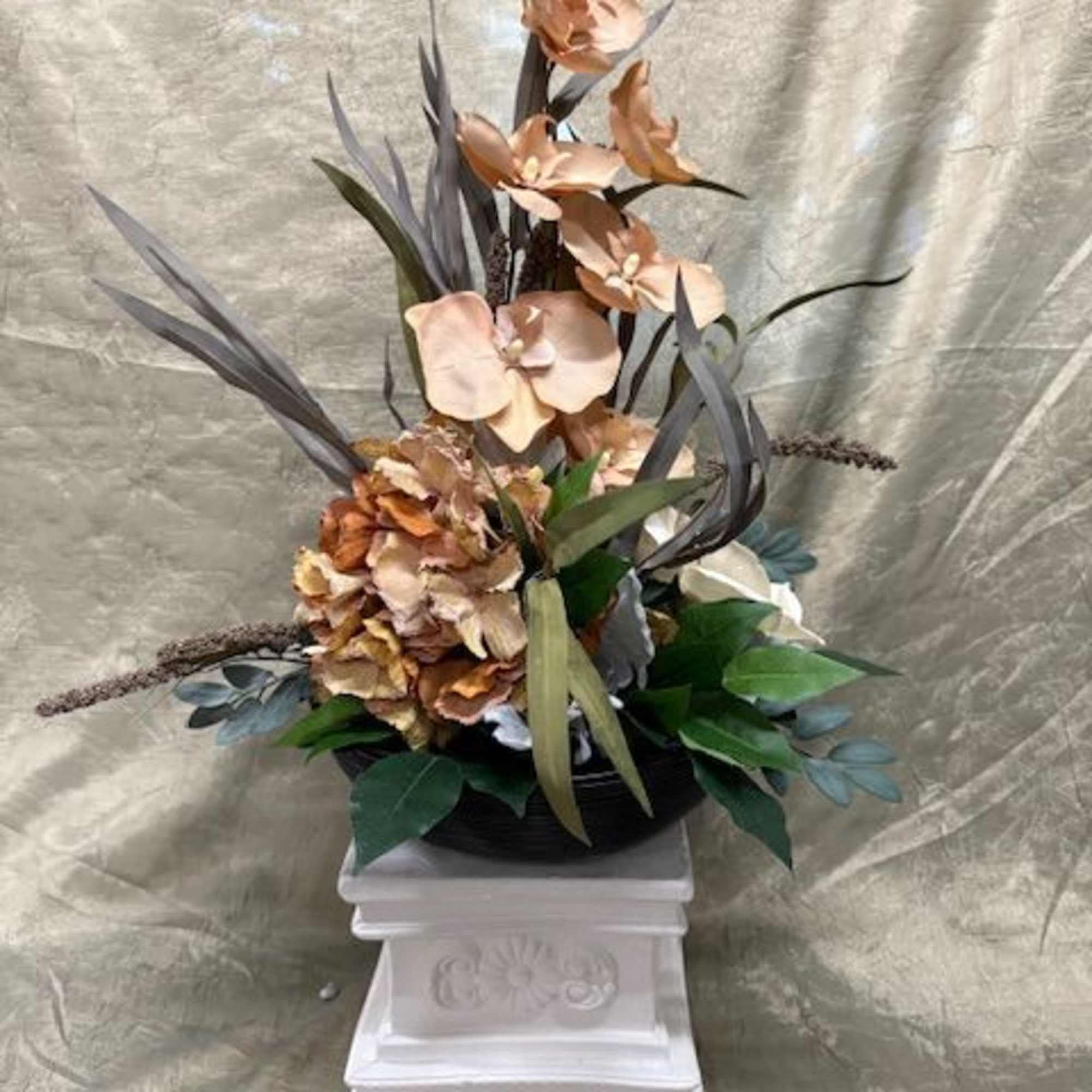 Tall floral arrangement with peach orchids and dried hydrangea in a white pedestal vase