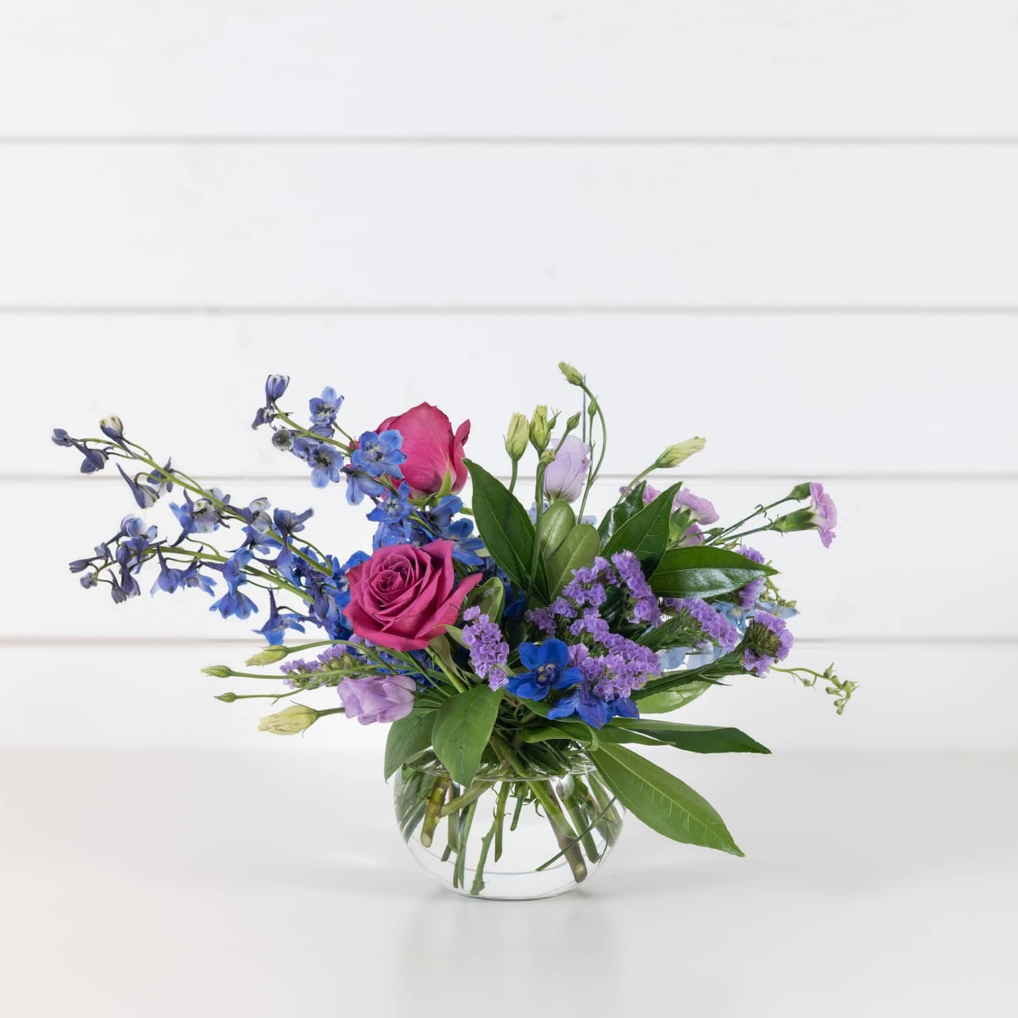 Pink roses and purple-blue flowers in a clear glass vase