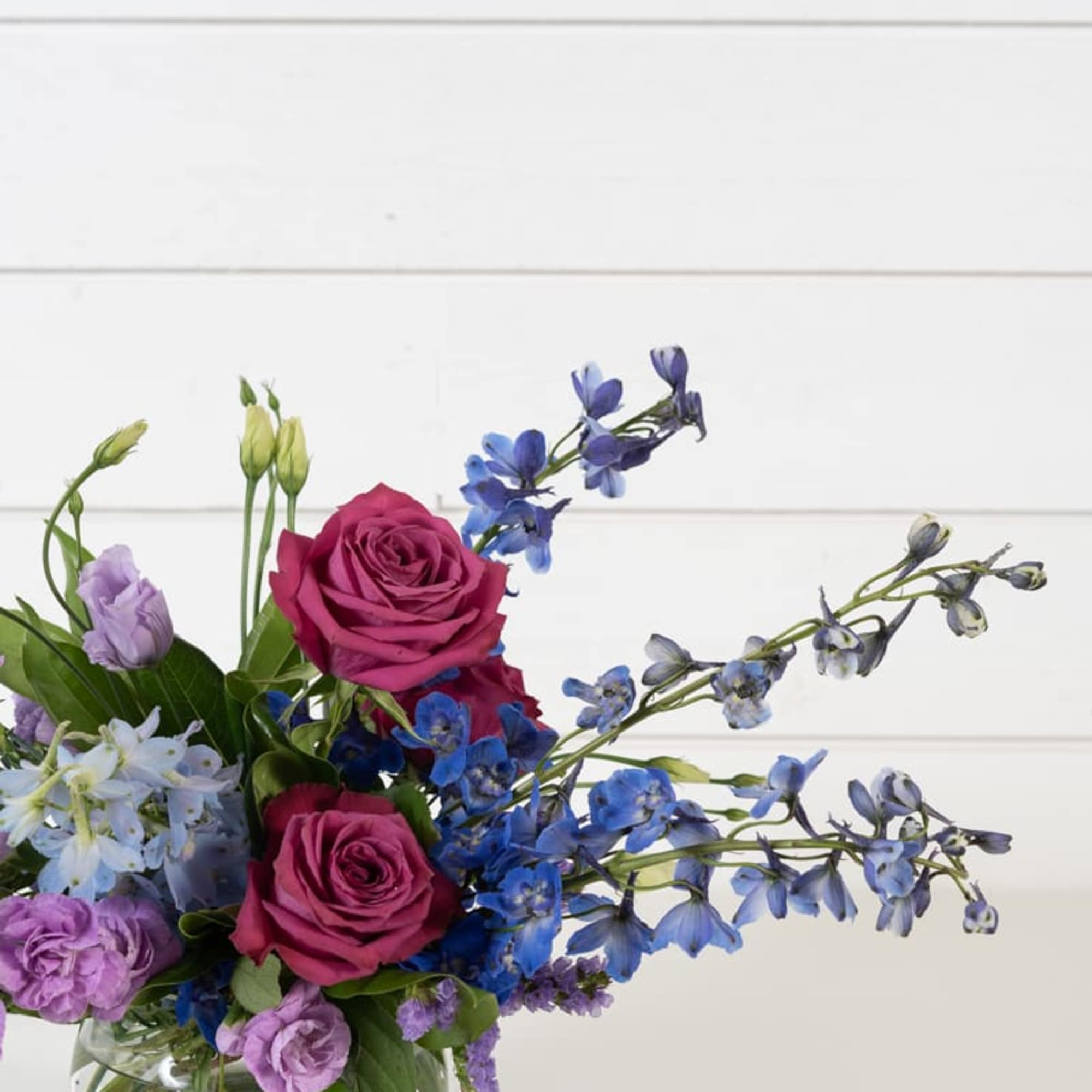 Bouquet of pink roses and blue flowers in a clear glass vase