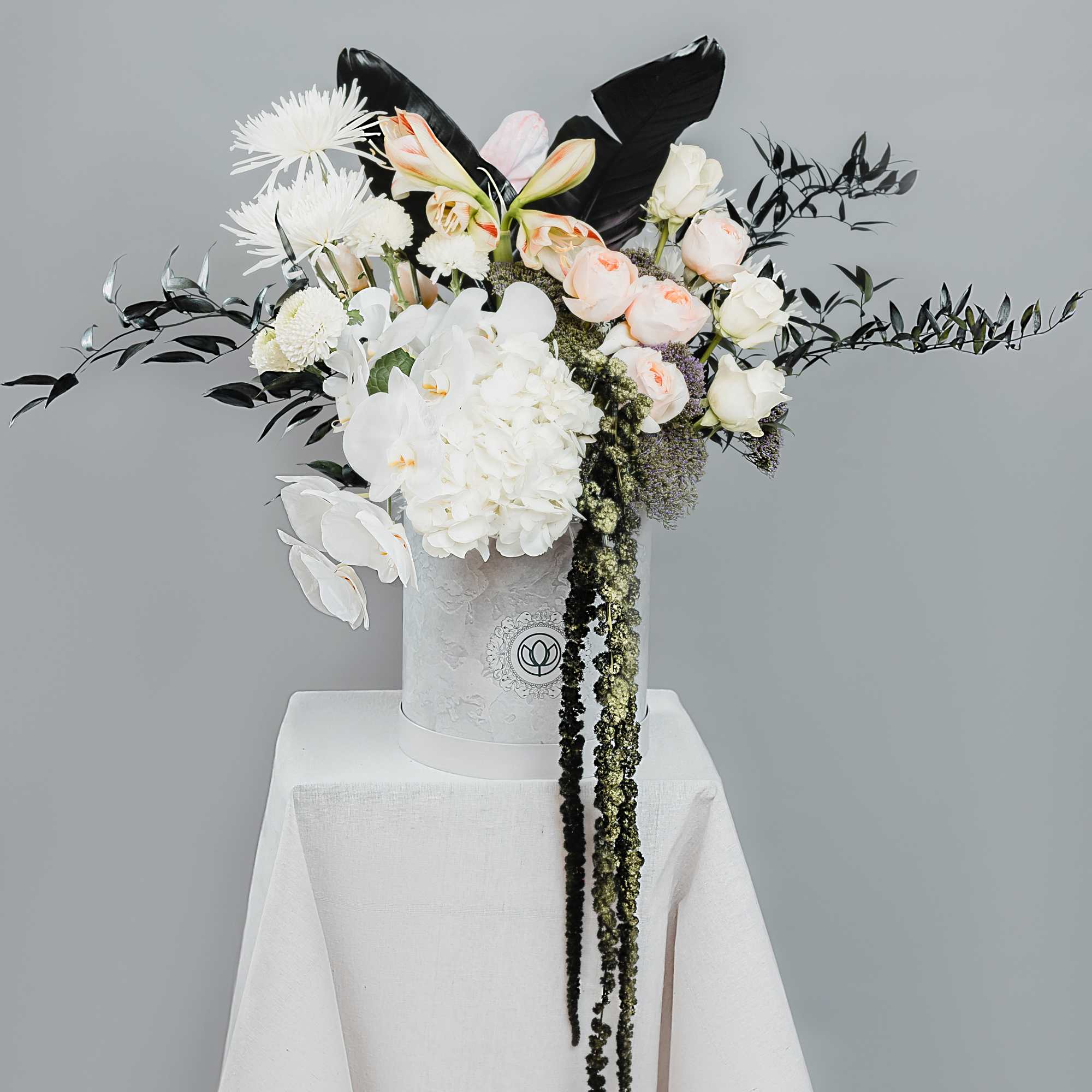 White and blush floral arrangement in a white hatbox on a draped pedestal