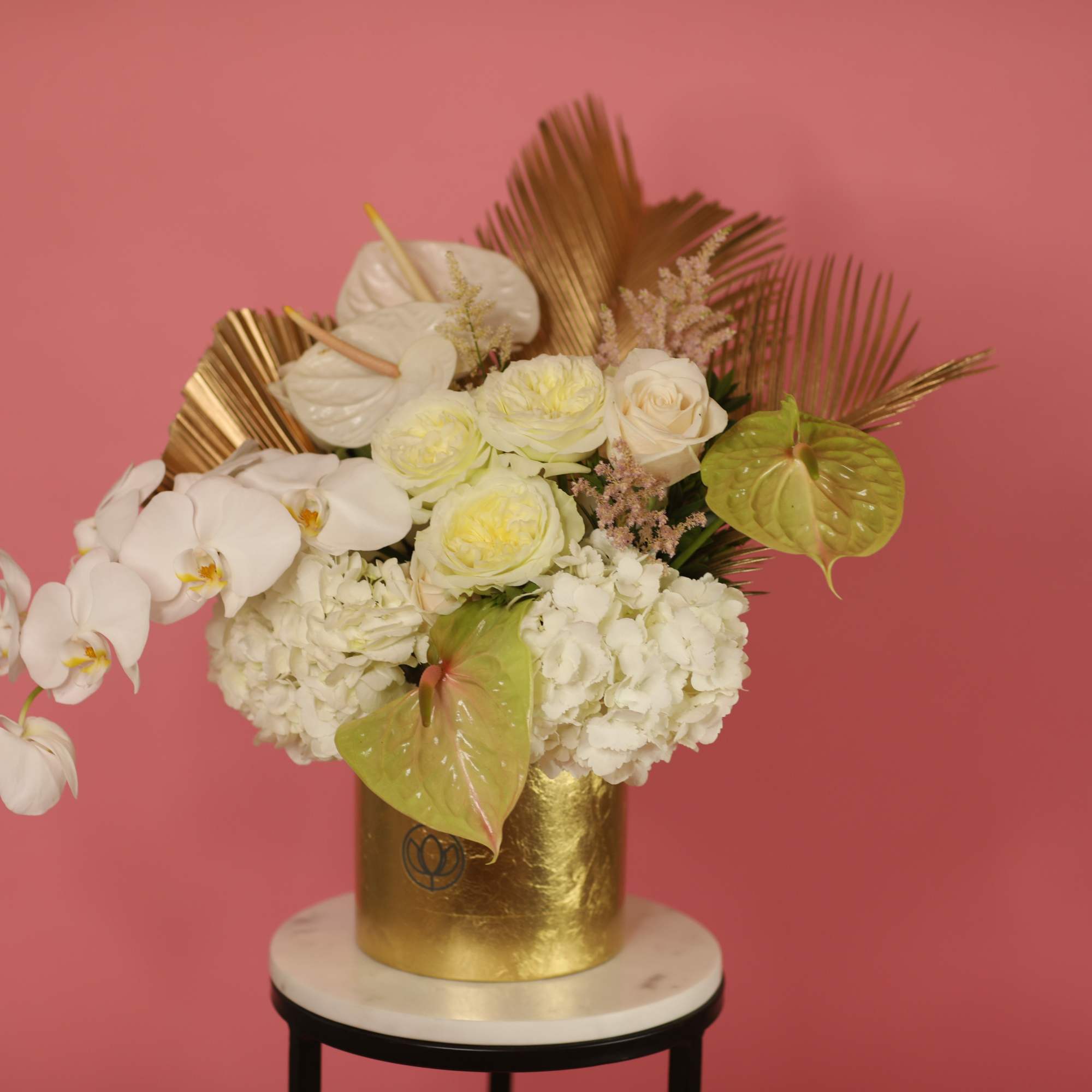 White orchids and roses in a gold vase with tropical leaves