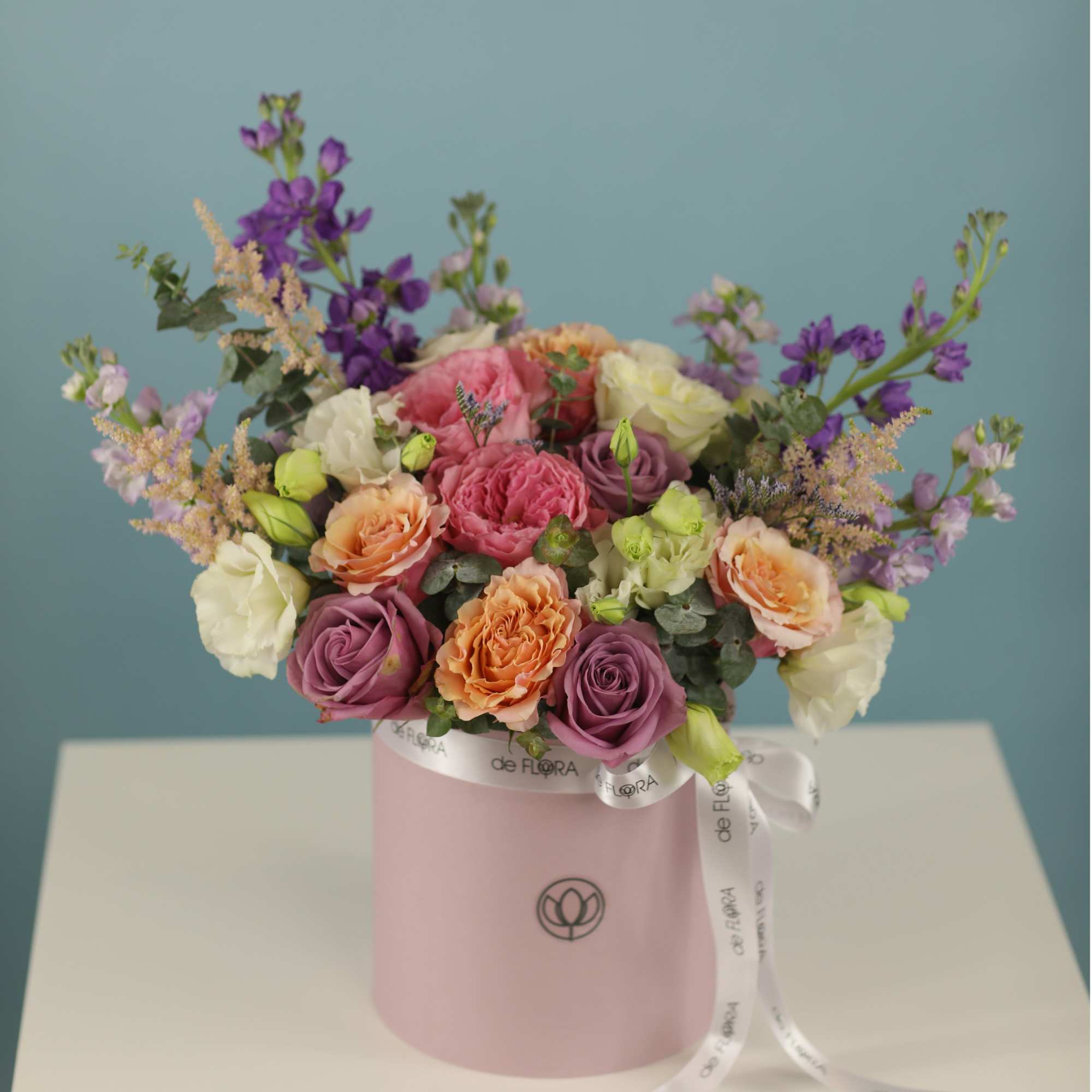 Mixed bouquet of pink, peach, white, and purple flowers in a pink box