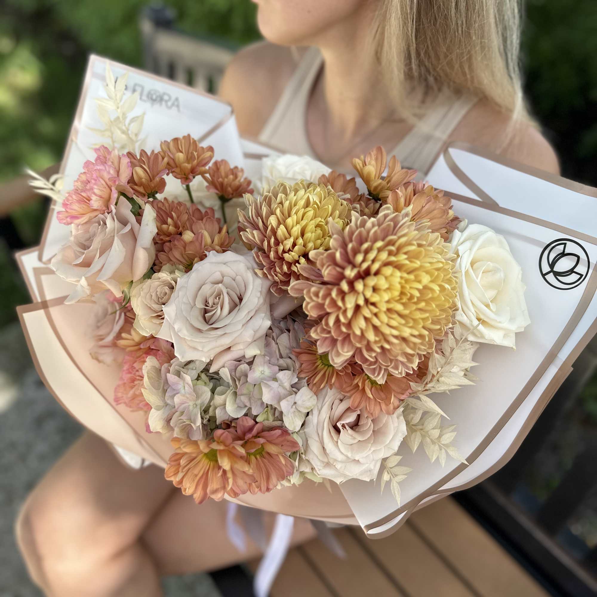 Hand-tied bouquet of blush roses and peach chrysanthemums in white wrap