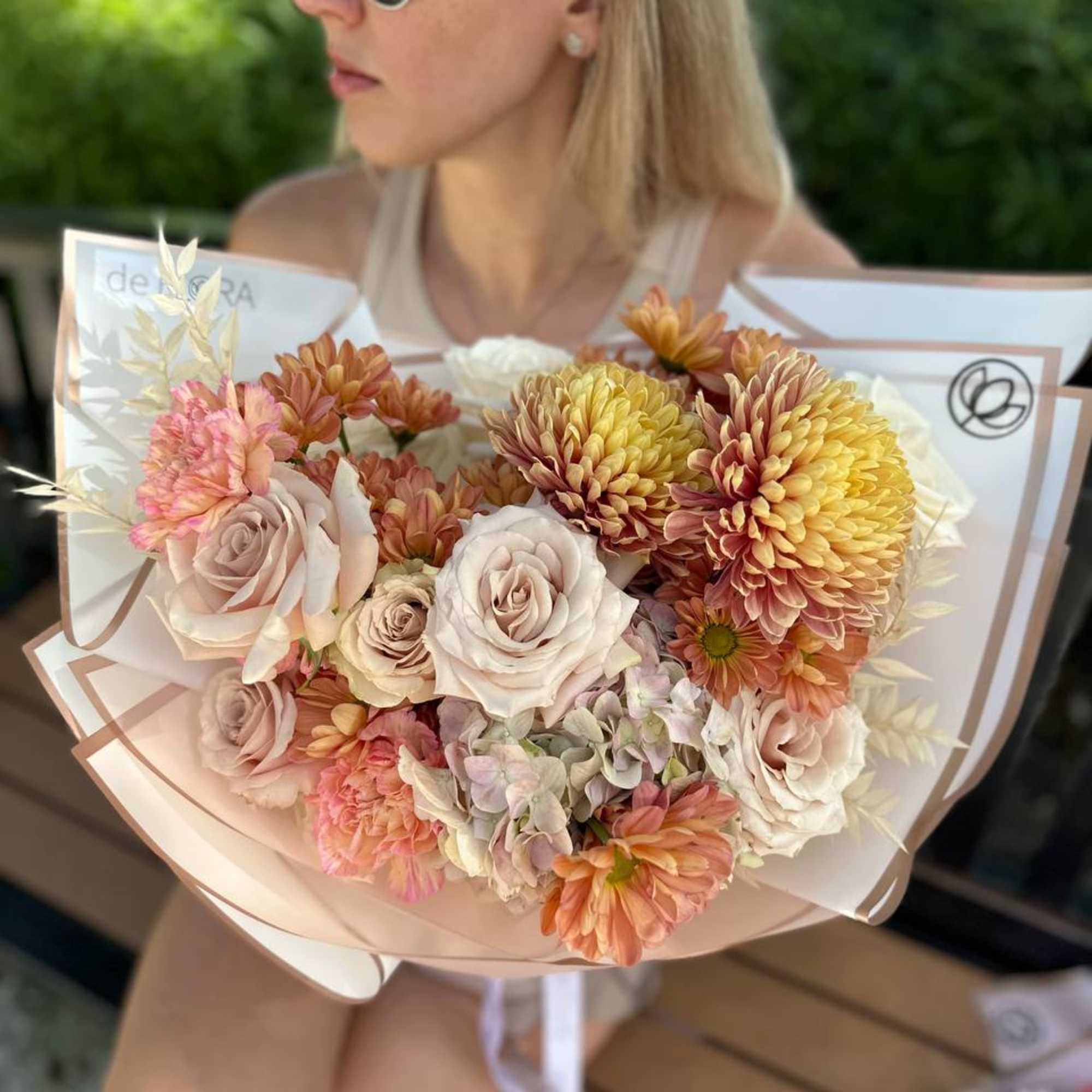 Woman holding a pastel bouquet of roses and chrysanthemums wrapped in paper