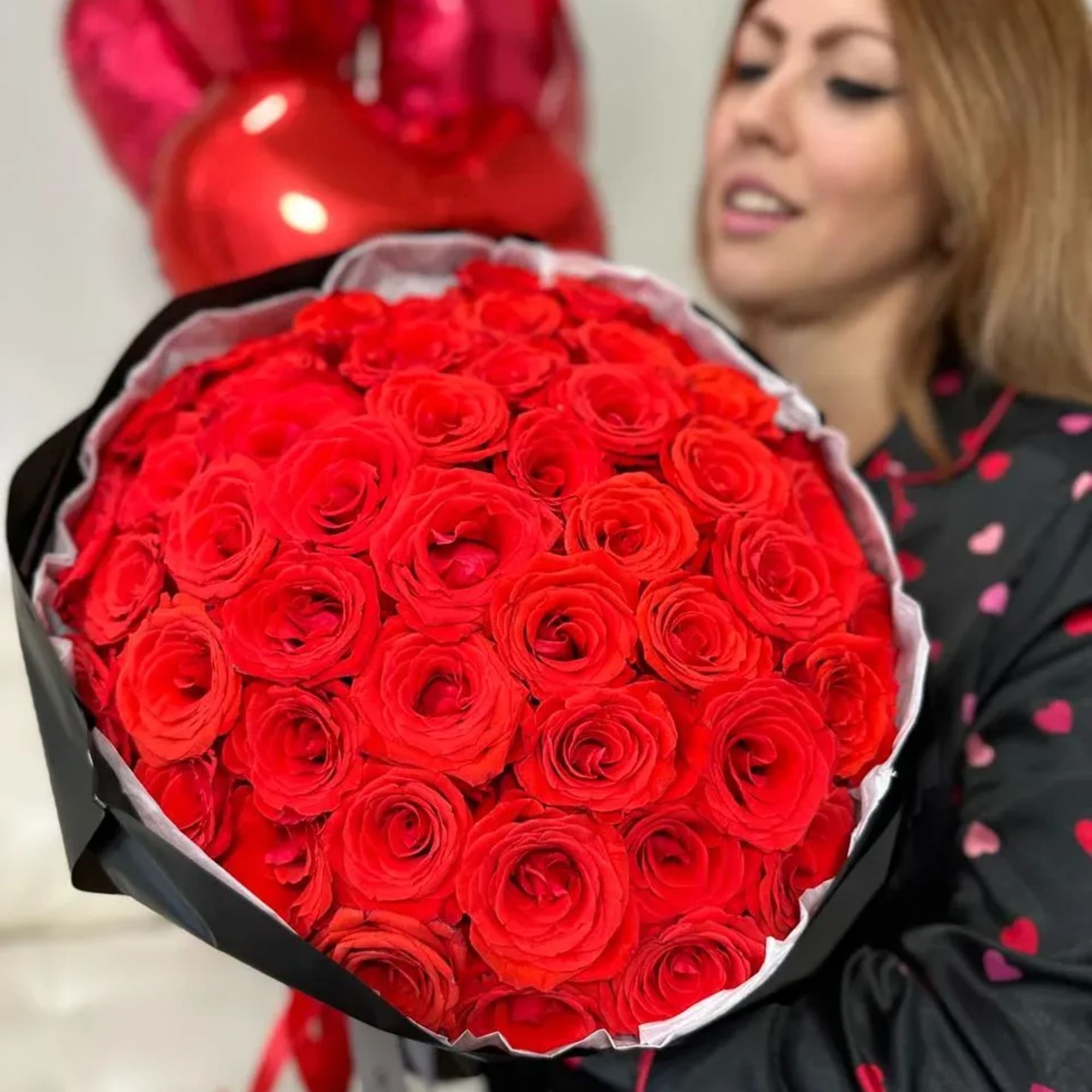 Large bouquet of red roses with heart balloons behind it