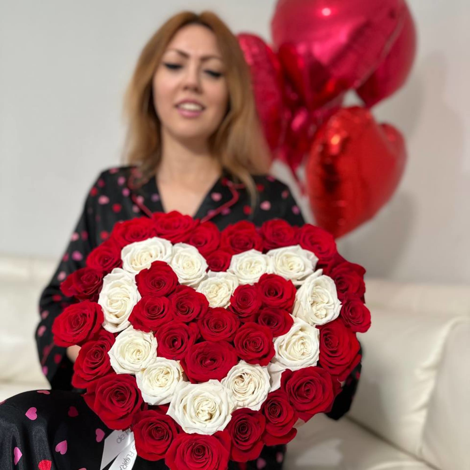 Heart-shaped bouquet of red and white roses with red heart balloons behind it