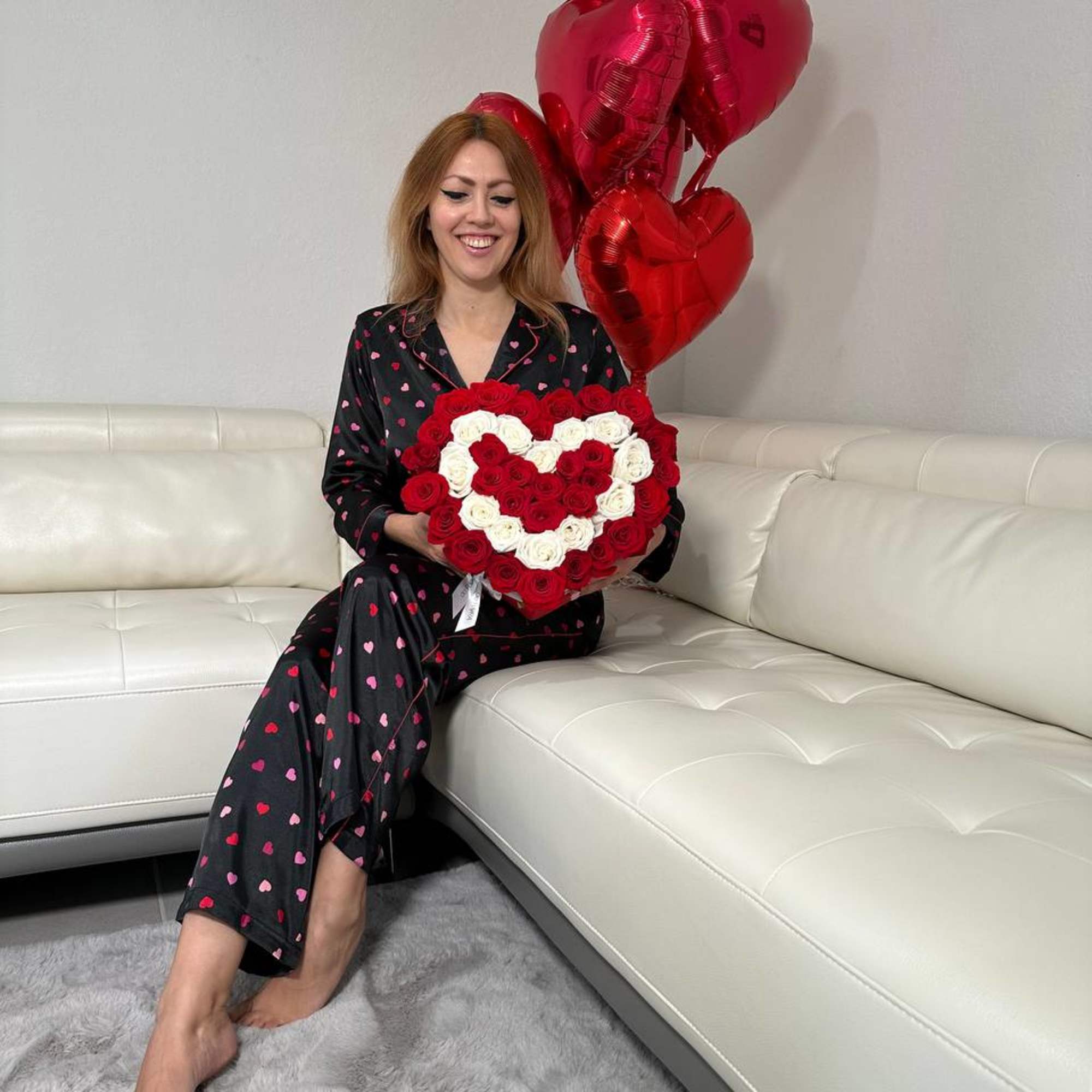 Woman holding a heart-shaped rose arrangement with red heart balloons