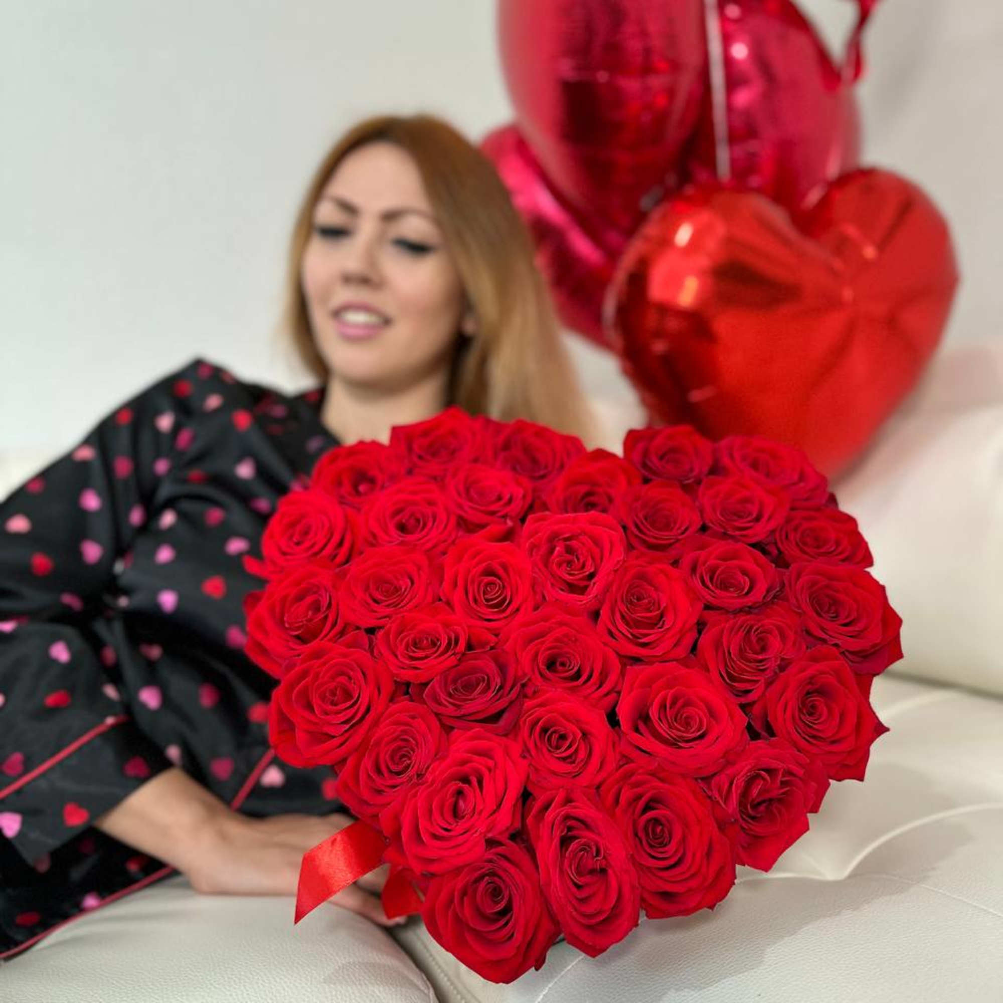 Heart-shaped bouquet of red roses with red heart balloons behind it