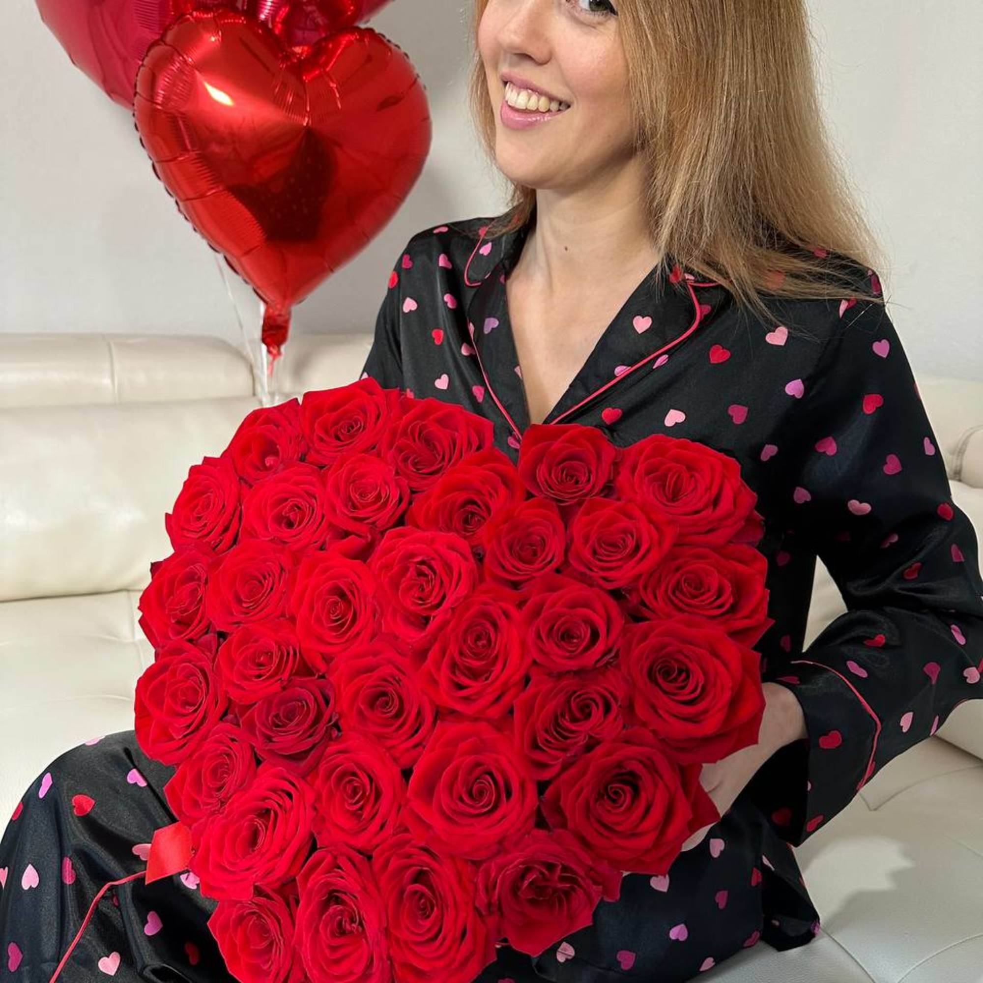 Woman holding a large heart-shaped bouquet of red roses with red heart balloons