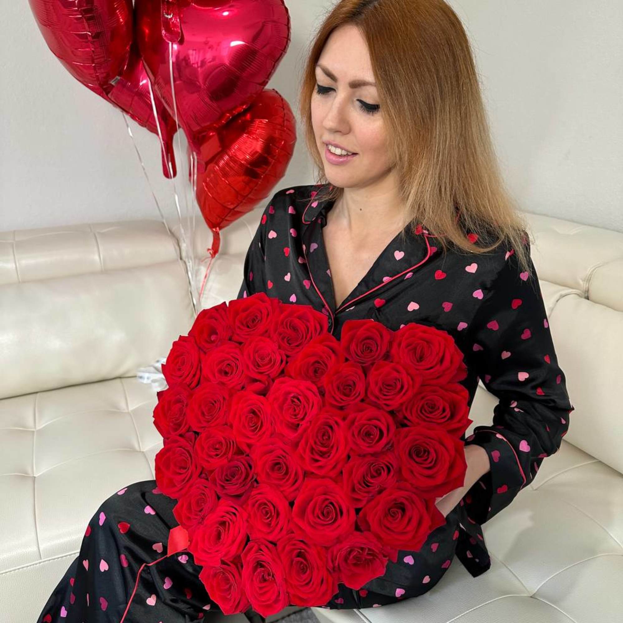 Woman holding a heart-shaped bouquet of red roses with red heart balloons
