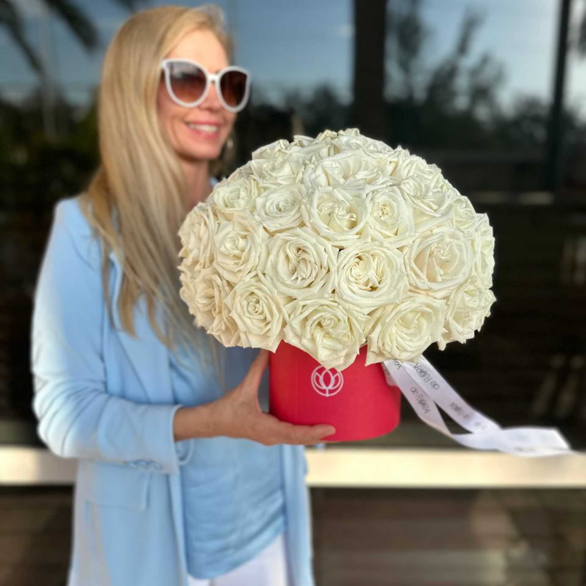 Woman holding a large white rose bouquet in a red hat box