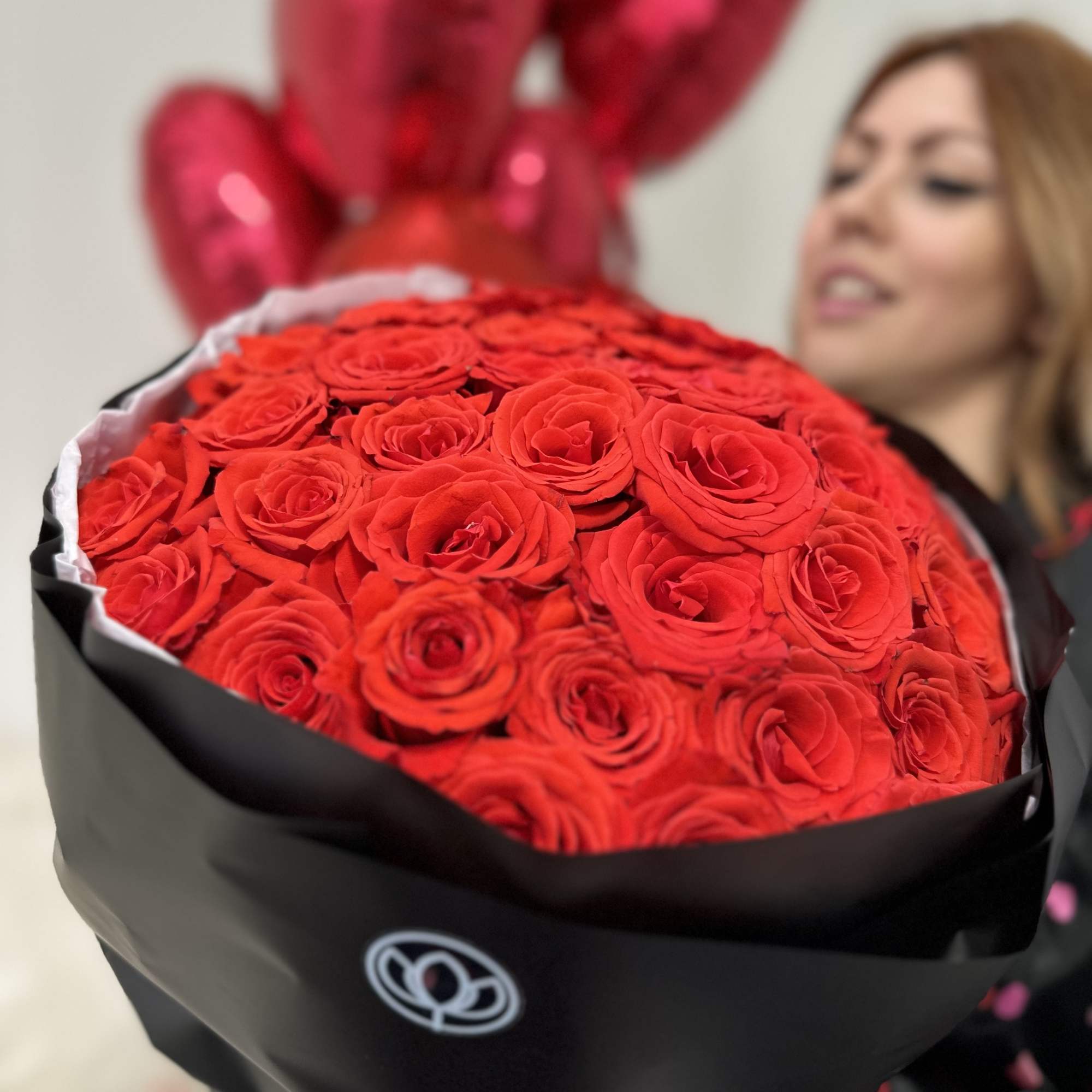 Large bouquet of red roses wrapped in black paper with red balloons behind it