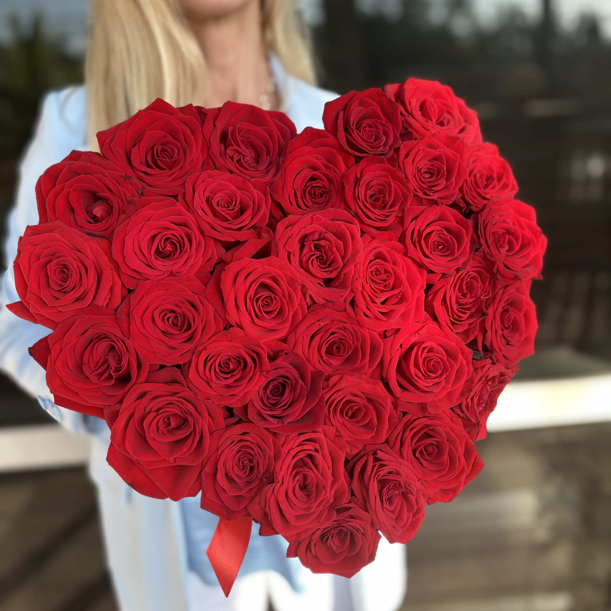 Heart-shaped bouquet of red roses held by a woman