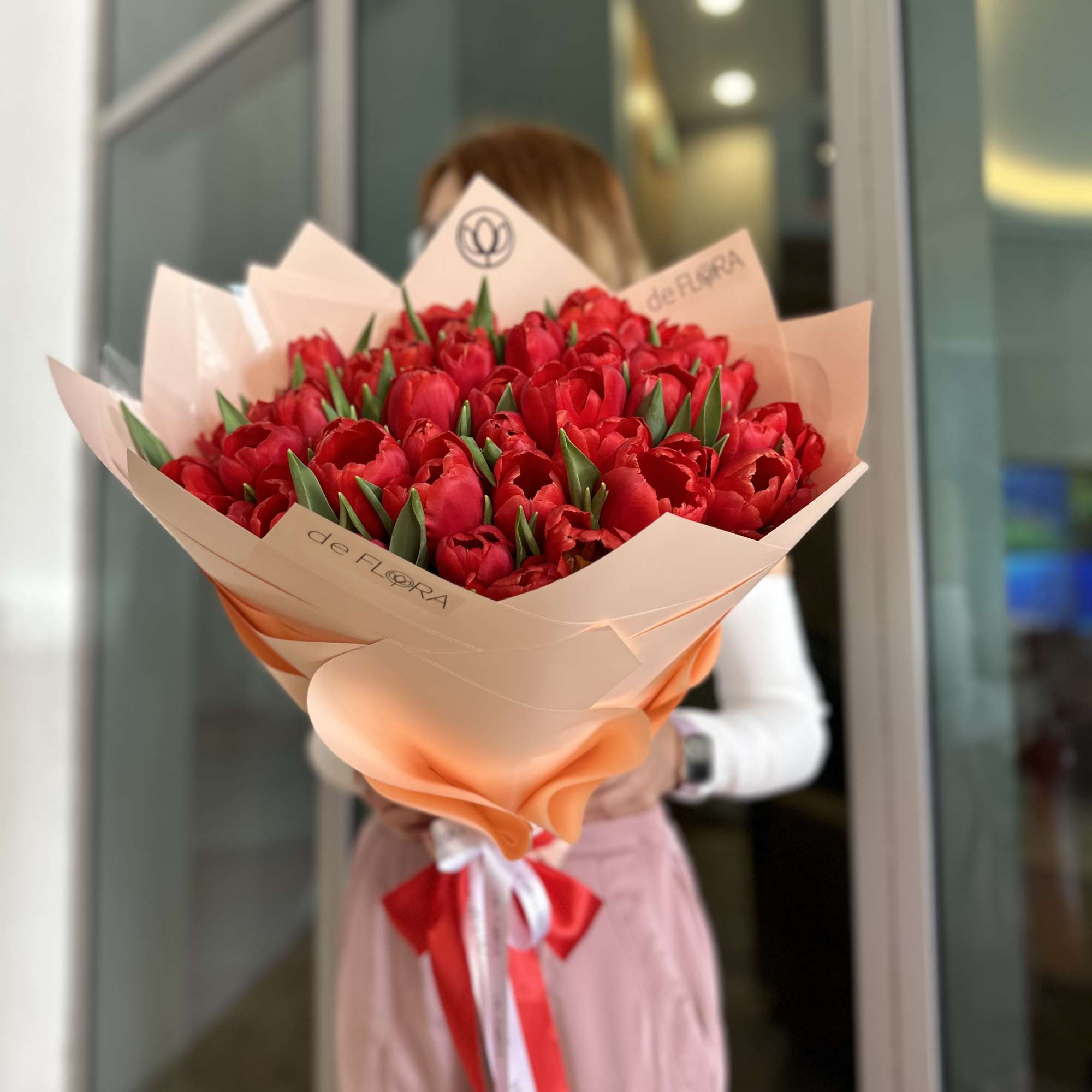 Large bouquet of red tulips wrapped in peach paper with a ribbon