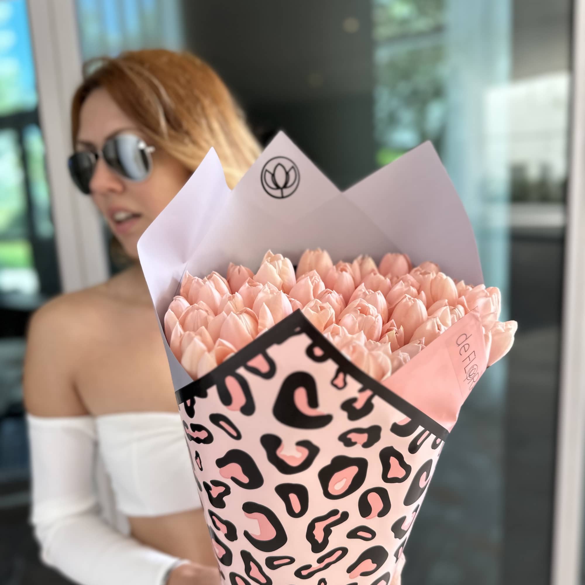 Woman holding a bouquet of pale pink tulips wrapped in leopard-print paper