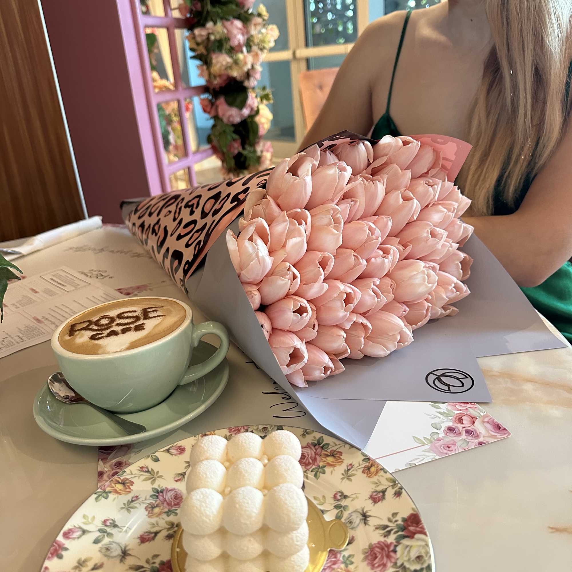 Bouquet of pale pink tulips wrapped in patterned paper beside a coffee cup