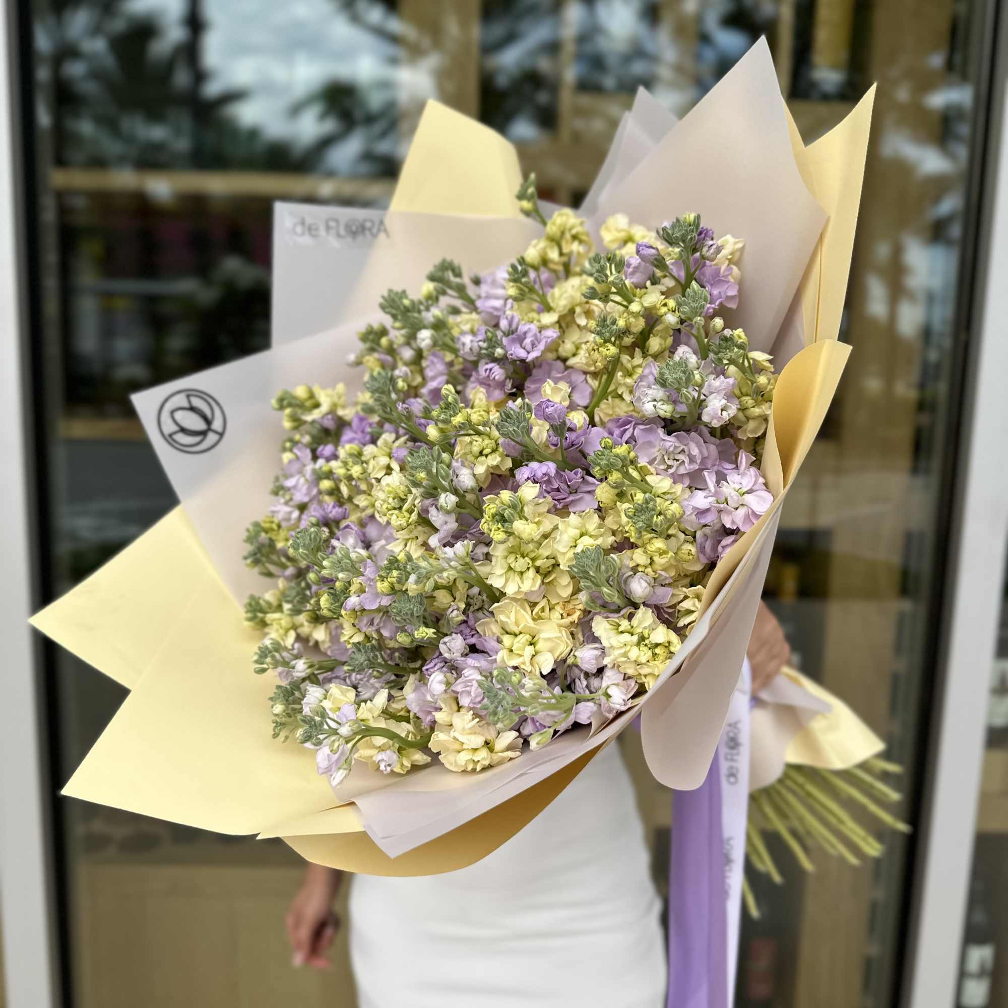 Large bouquet of pale yellow and lavender flowers wrapped in cream paper