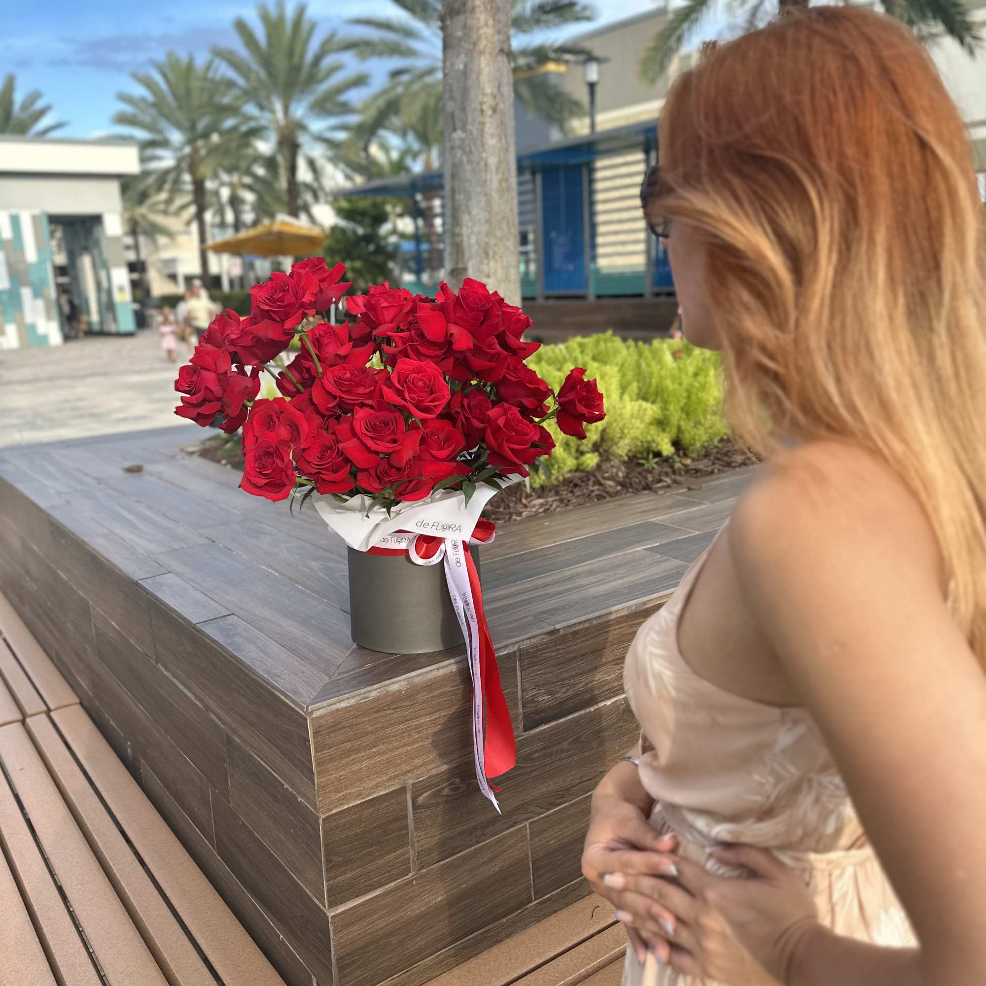 Large bouquet of red roses in a round box held by a woman outdoors