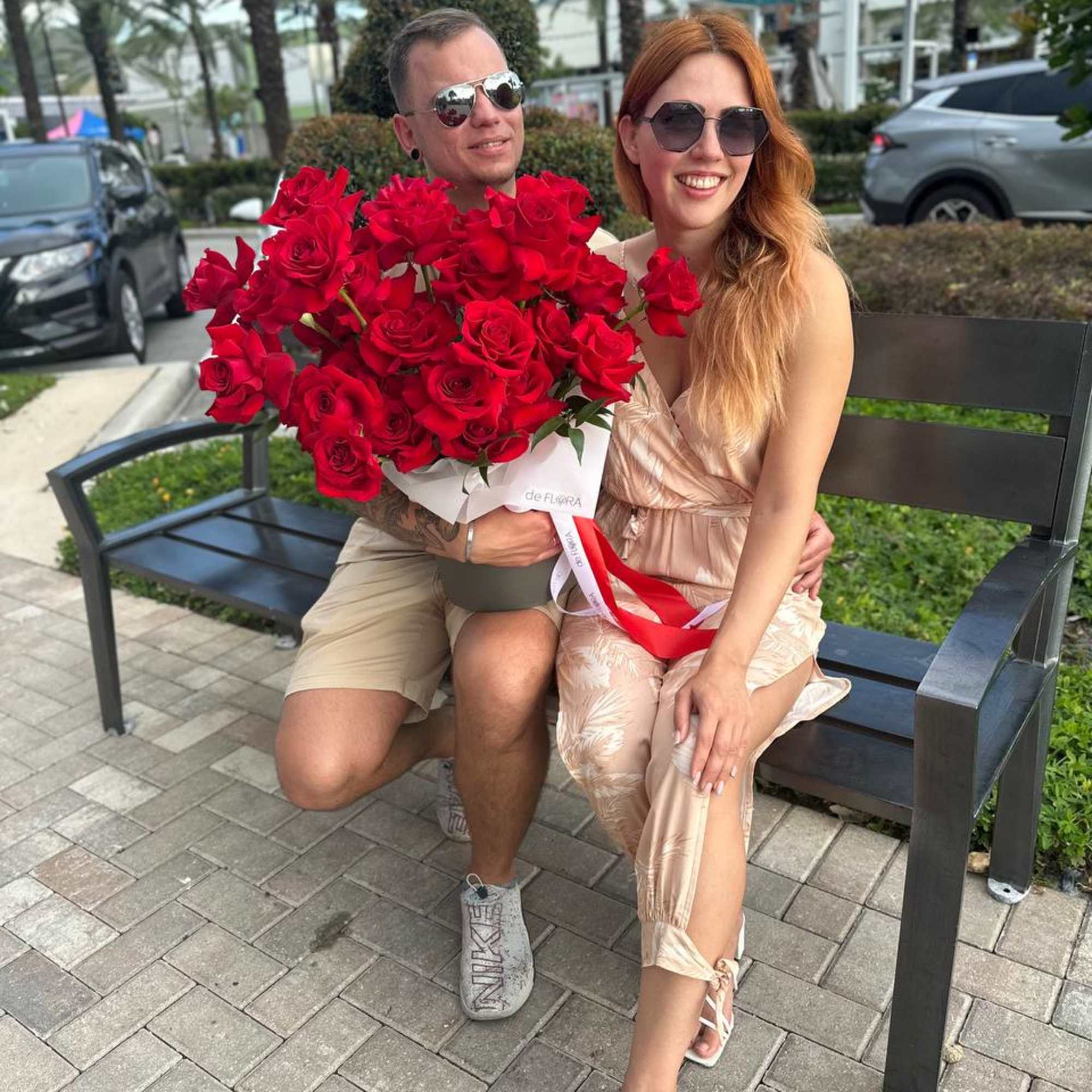 Couple sitting on a bench with a large bouquet of red roses