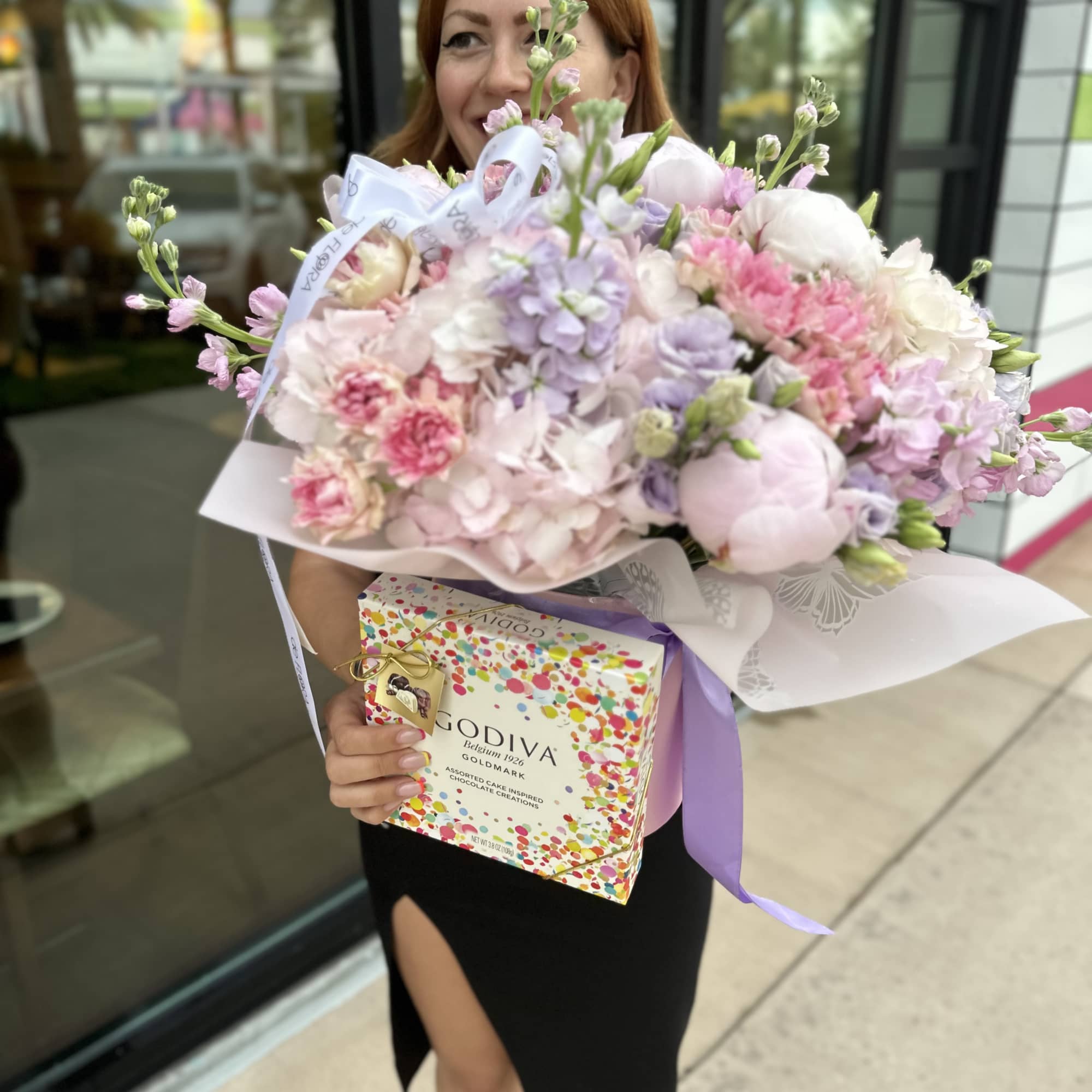 Woman holding a pastel bouquet and a Godiva chocolate box