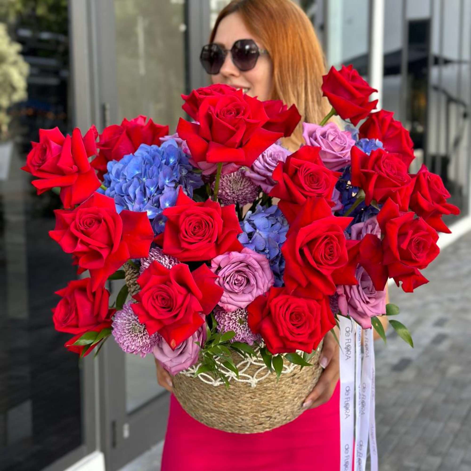 Large basket arrangement of red roses, blue hydrangeas, and lavender flowers