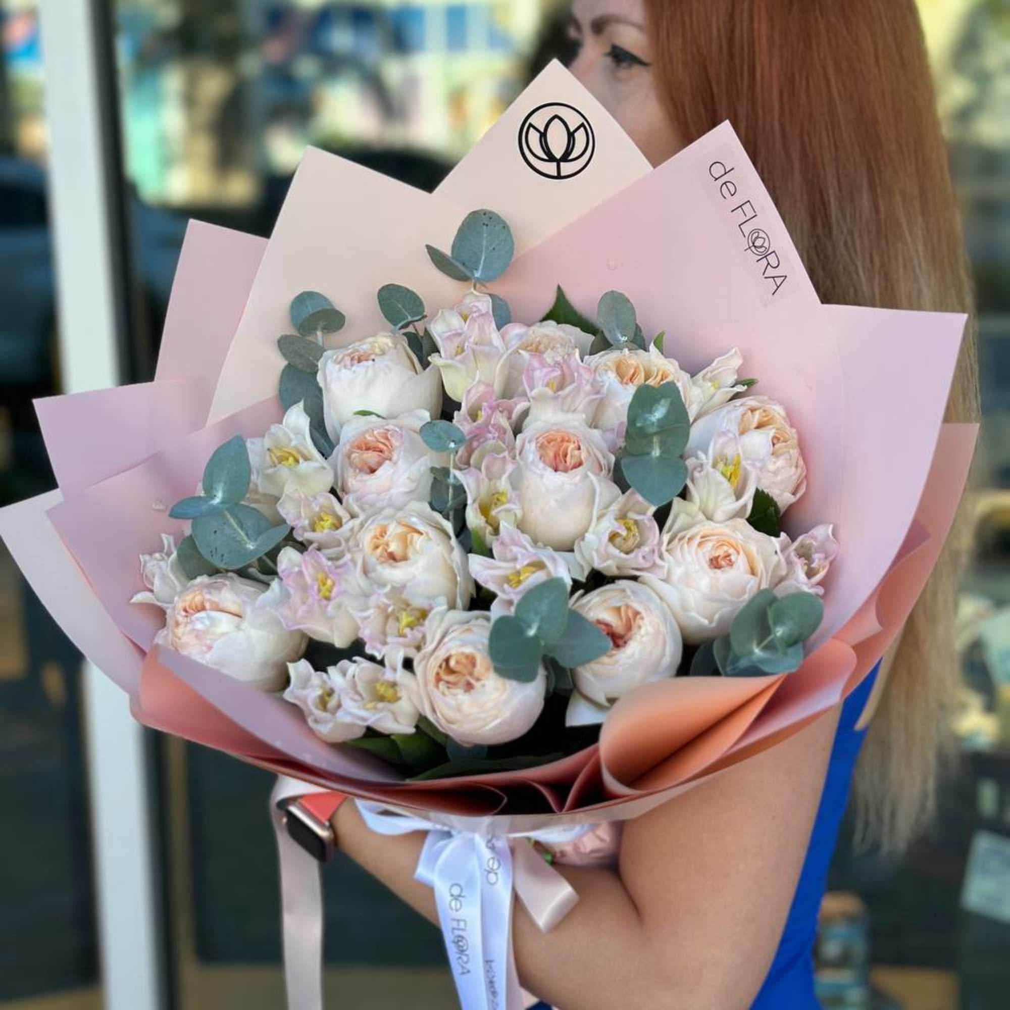 Woman holding a bouquet of pale pink and white flowers wrapped in pink paper