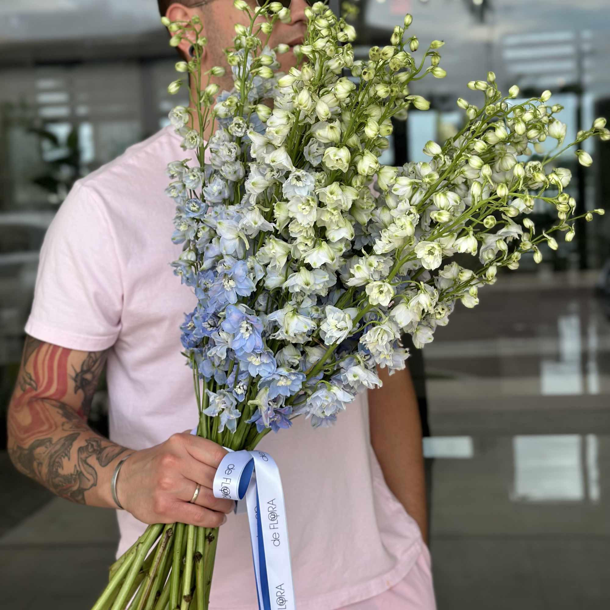 Man holding a large bouquet of pale blue and white flowers with a ribbon