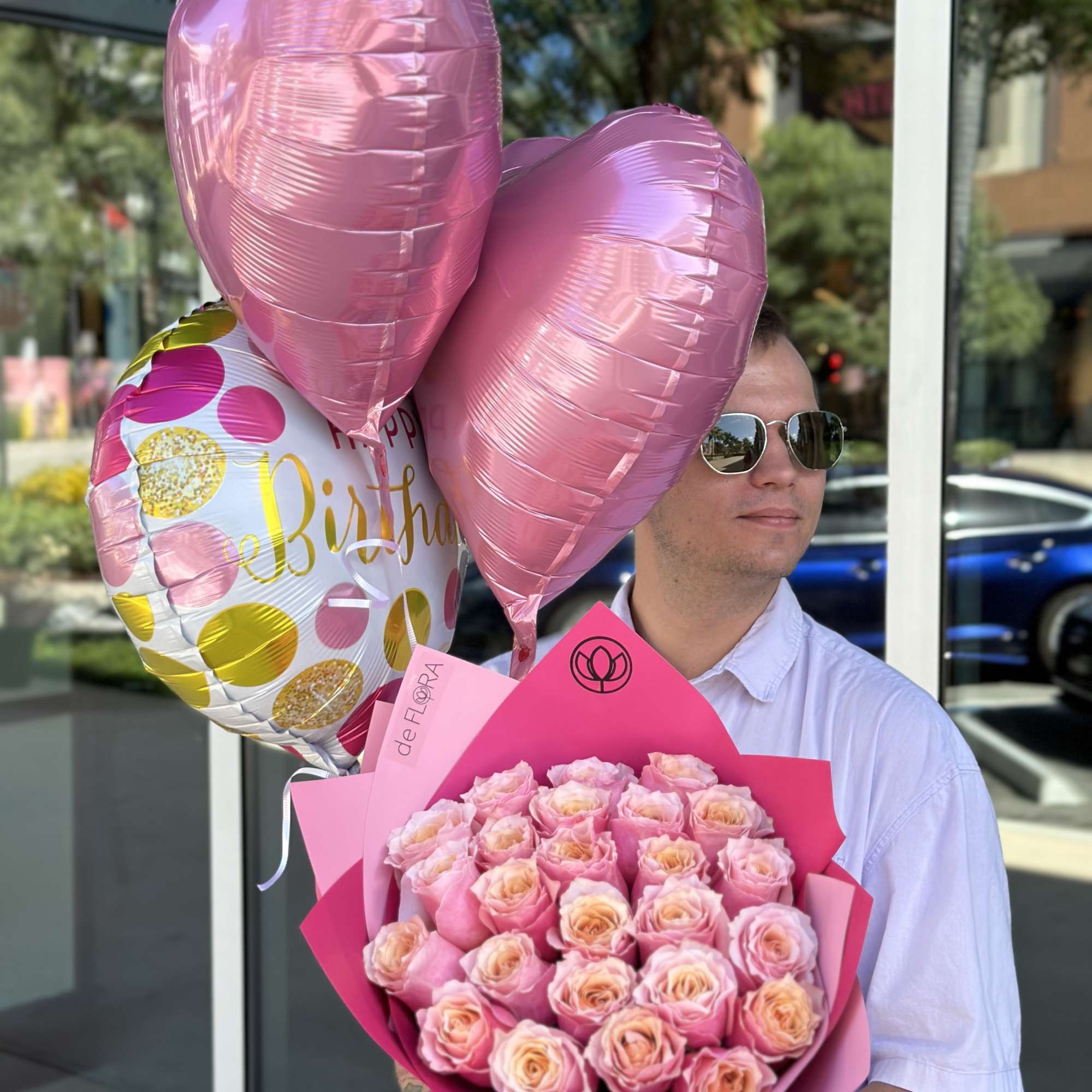 Man holding a pink rose bouquet with pink heart balloons