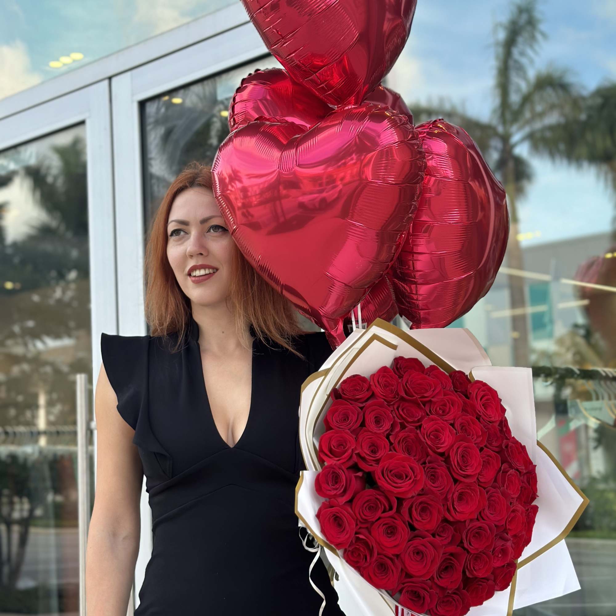 Woman holding a bouquet of red roses and red heart balloons