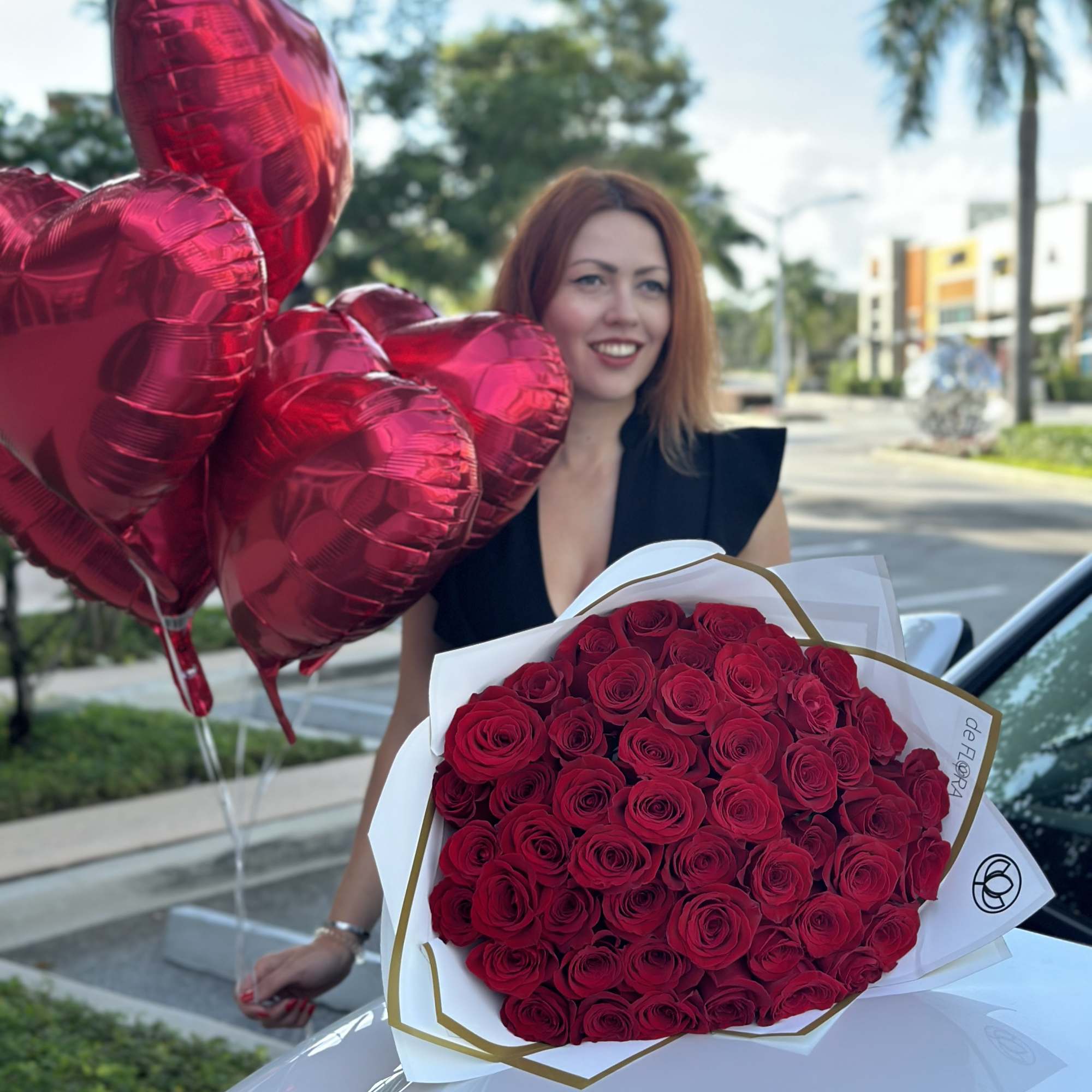 Woman holding a bouquet of red roses with red heart balloons