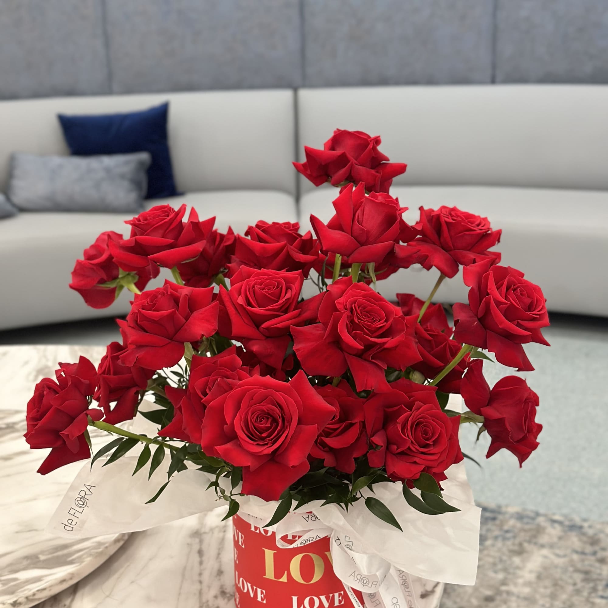 Red roses arranged in a round gift box with a white ribbon.