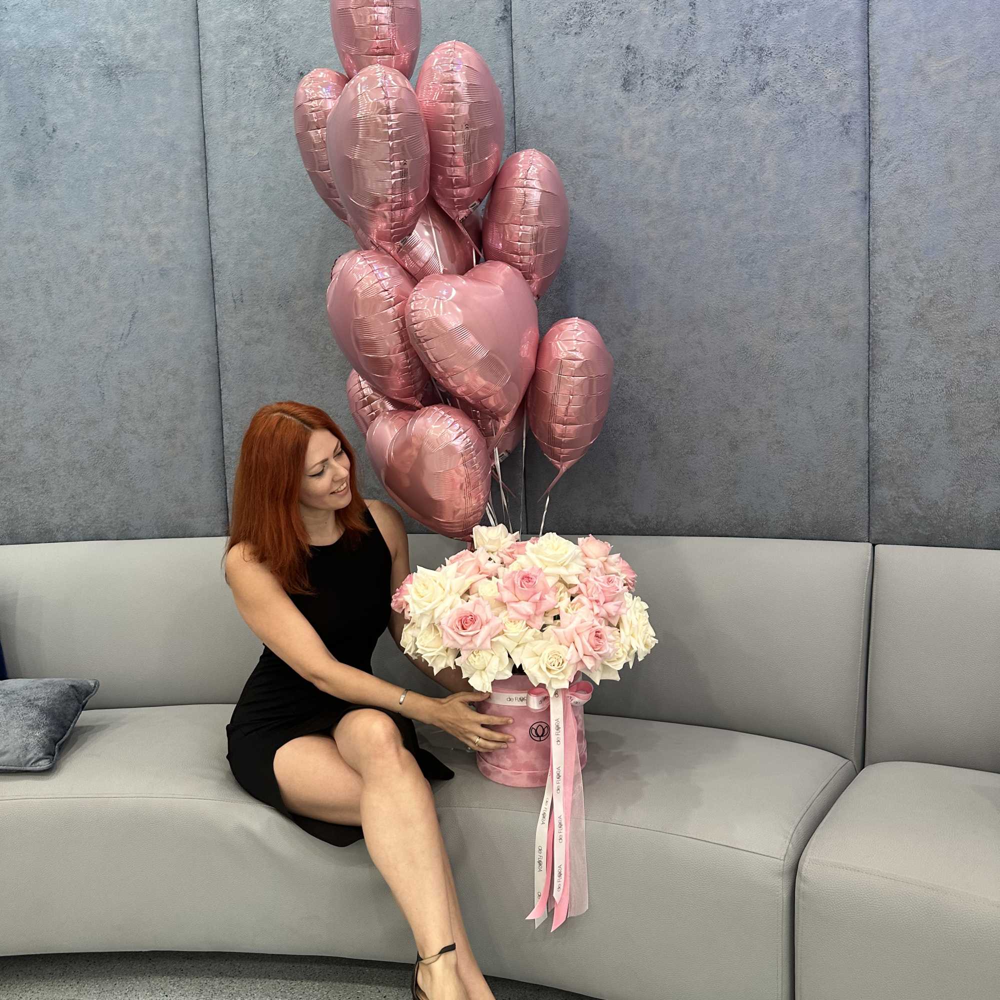 Pink heart balloons above a bouquet of pale roses in a pink box