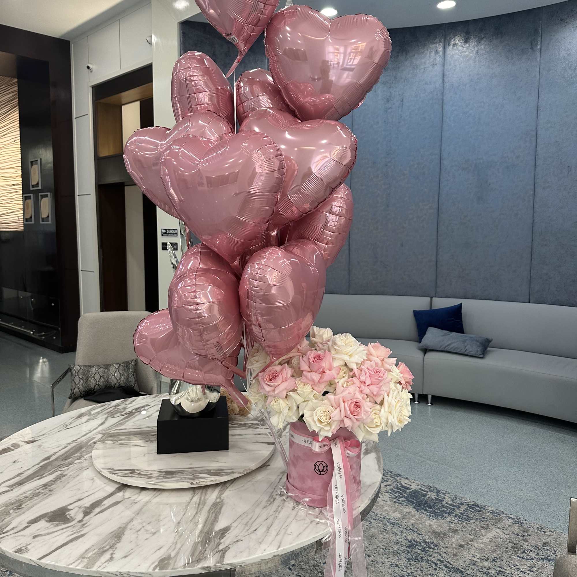 Pink heart balloons beside a bouquet of pink and white roses in a vase