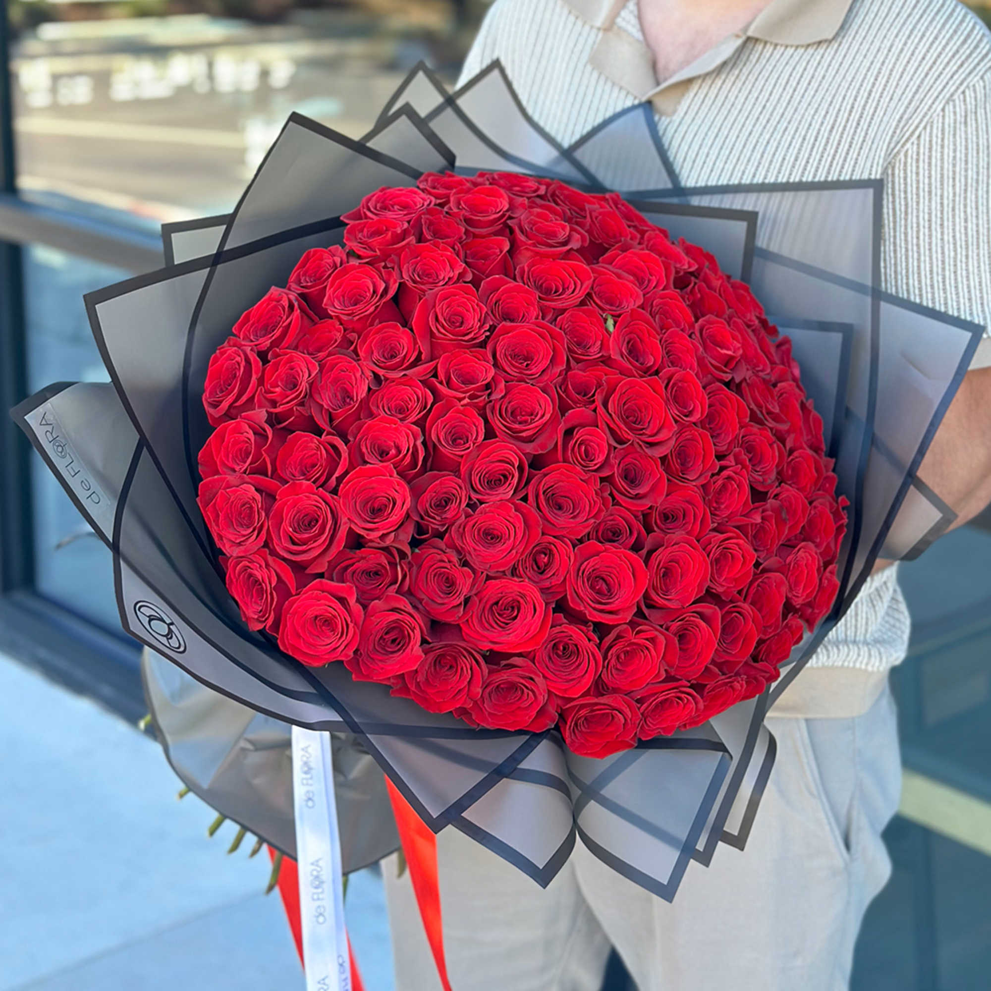 Extra-large bouquet of tightly packed red roses wrapped in black translucent paper with ribbons