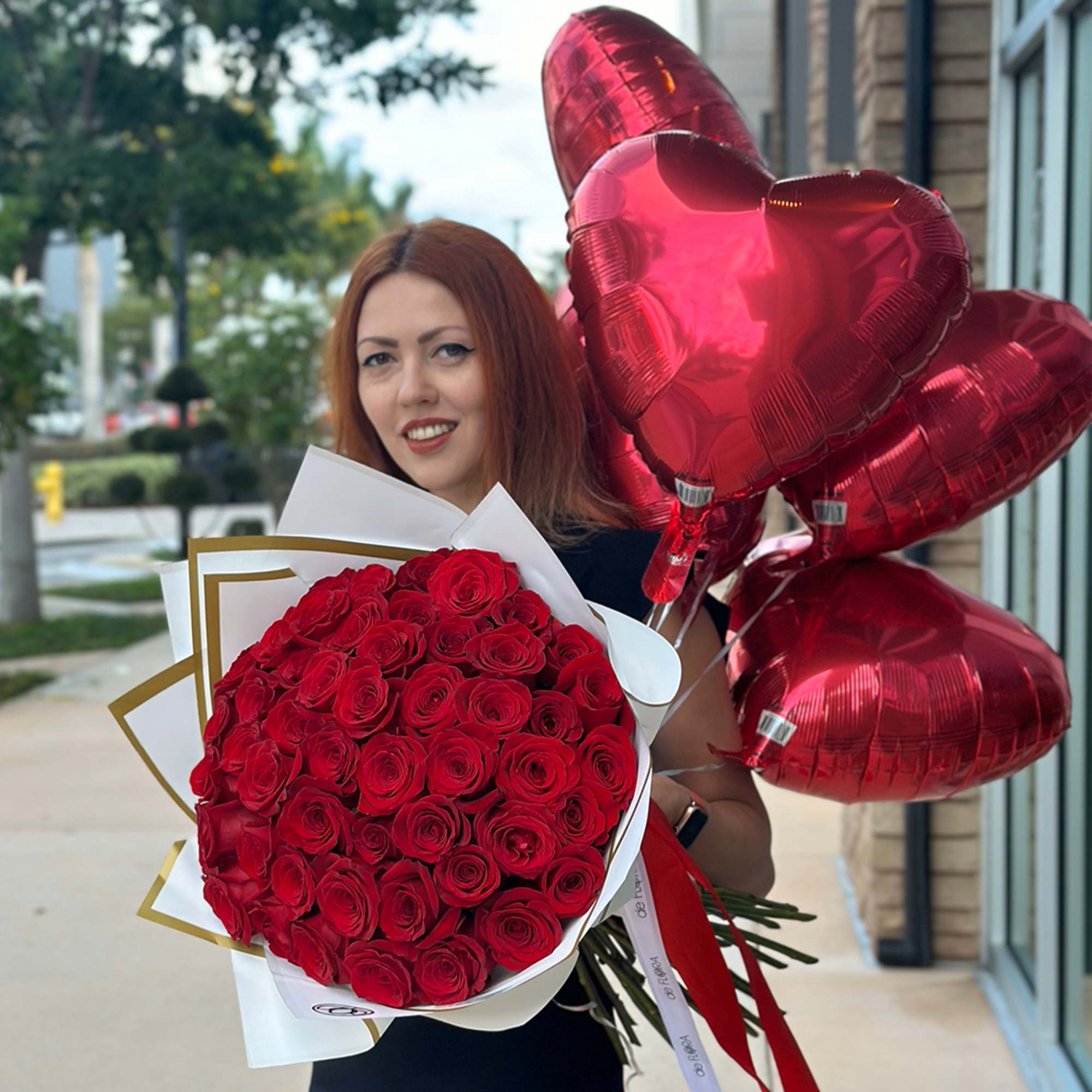 Woman holding a bouquet of red roses and red heart balloons