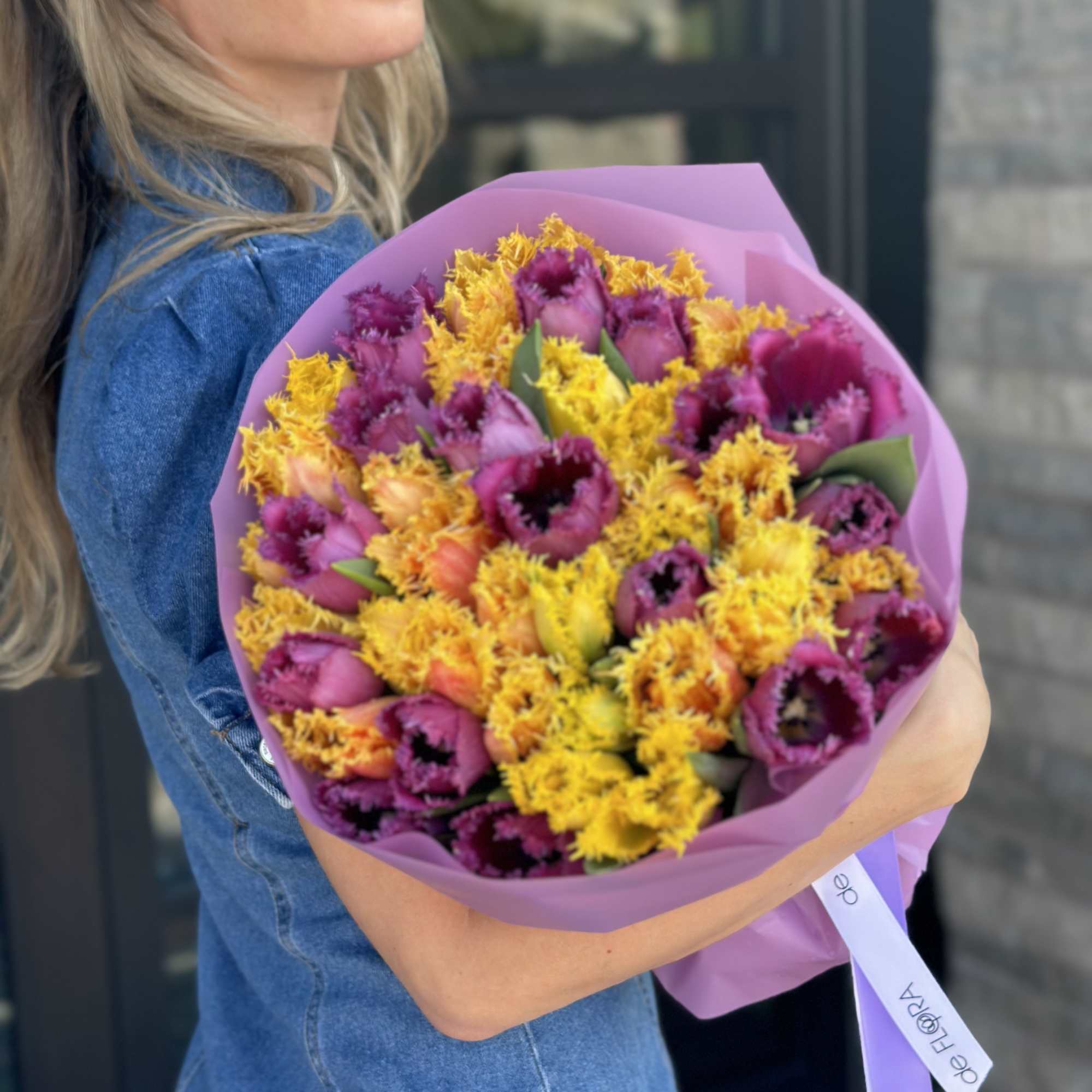 Woman holding a bouquet of purple and yellow tulips wrapped in pink paper