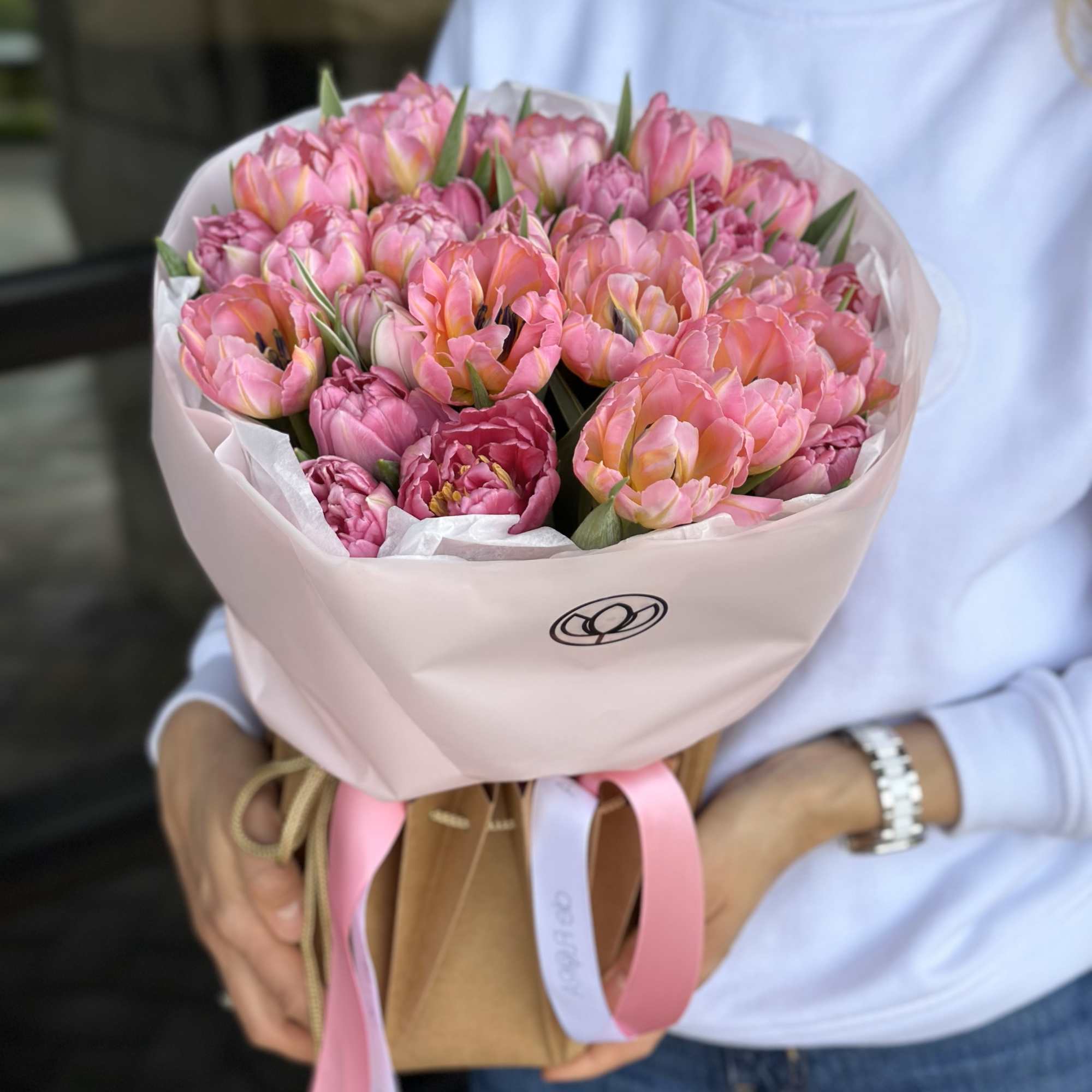 Pink tulip bouquet wrapped in pale pink paper and held by a person