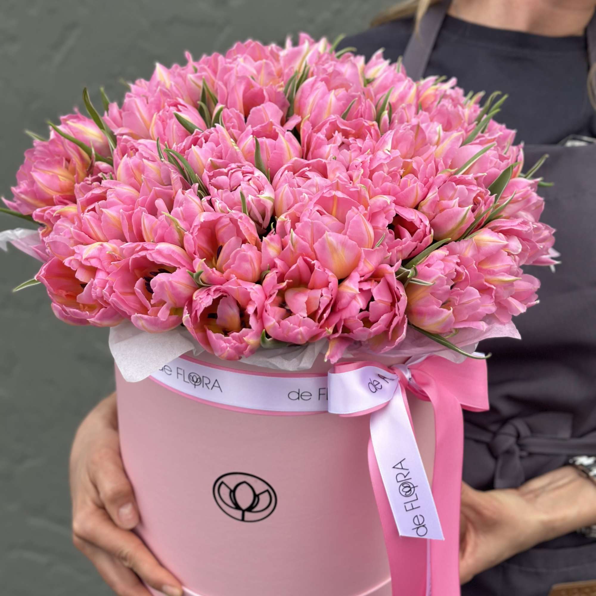 Pink tulips arranged in a round pink hat box with a ribbon